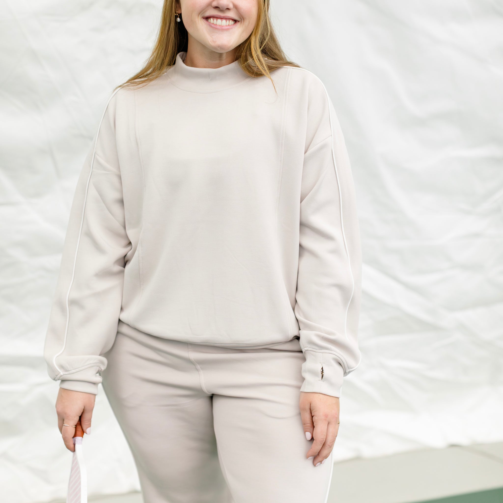 Woman wearing a beige track suit with white piping details.