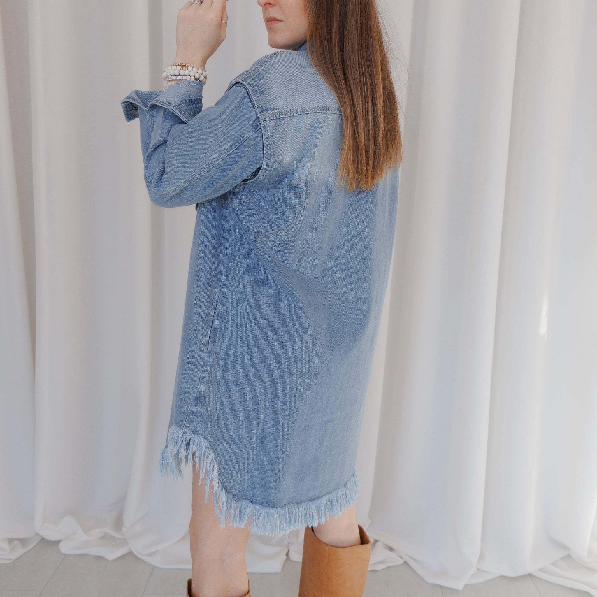 Person wearing a denim dress with a white curtain background