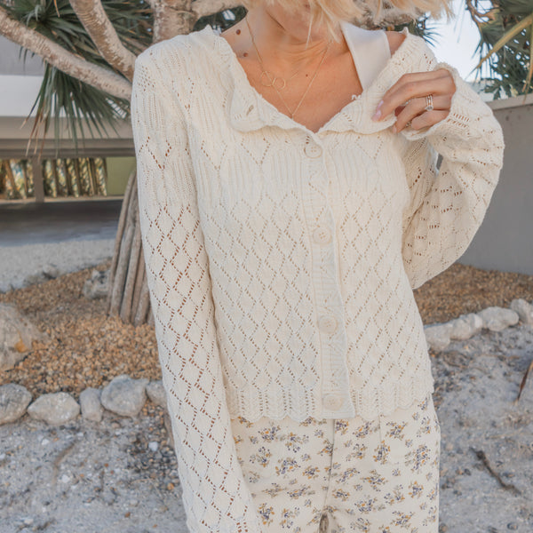 Person wearing a cream-colored knitted cardigan with a blurred natural background