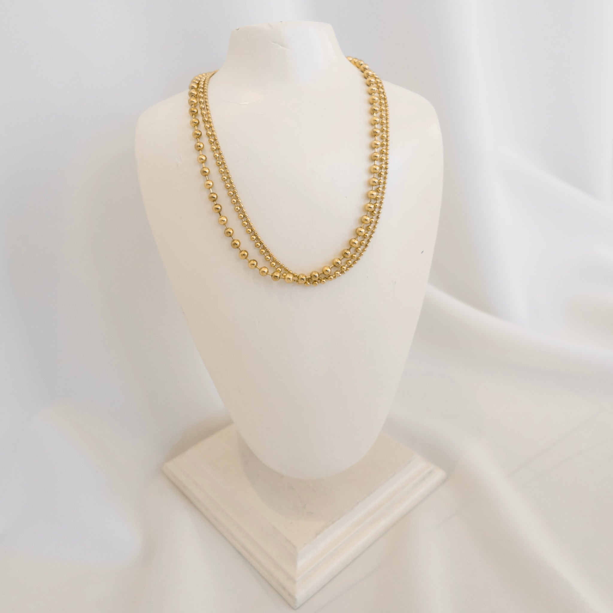 Gold chain necklace on a mannequin bust against a white background