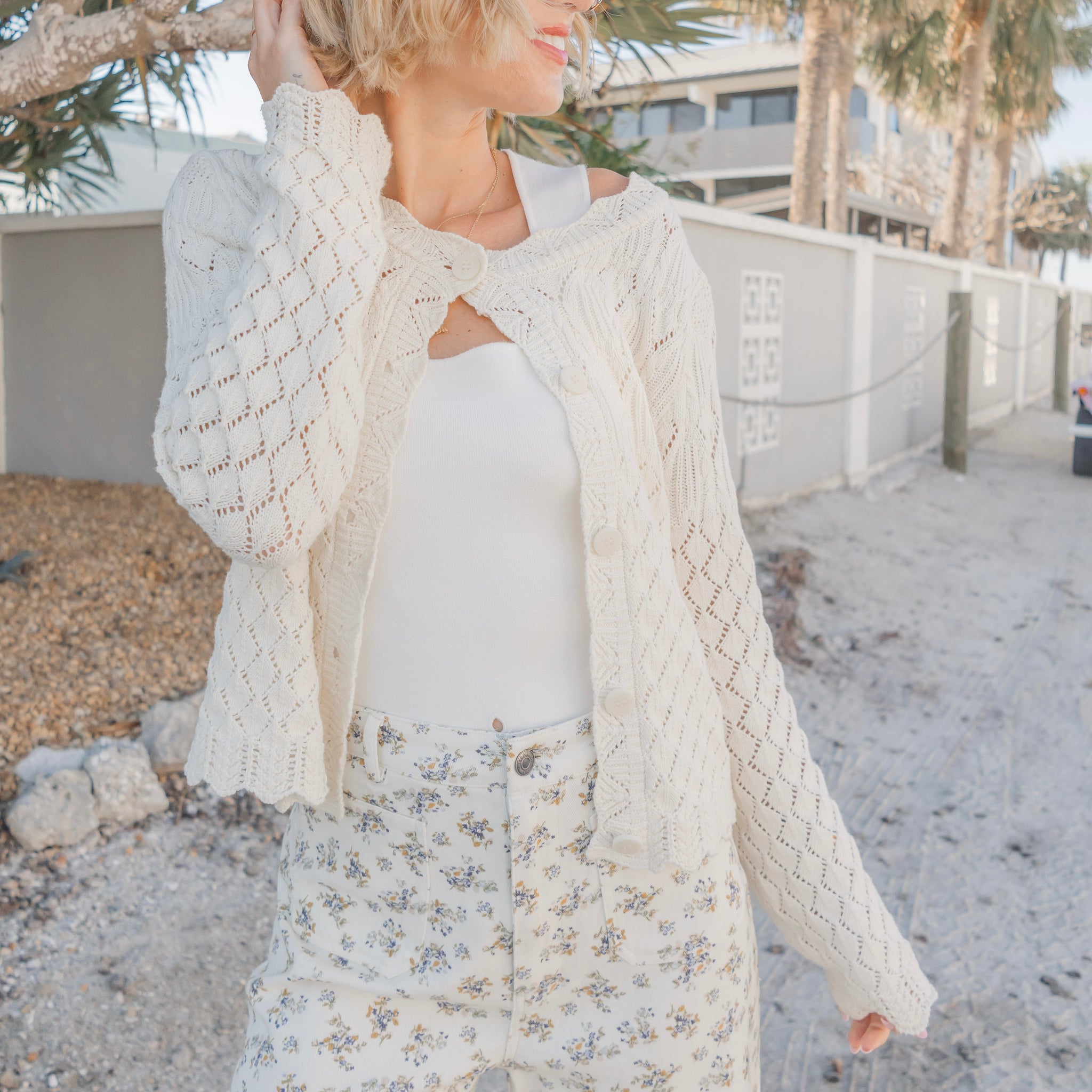 Woman wearing a white cardigan over a floral dress on a beach.