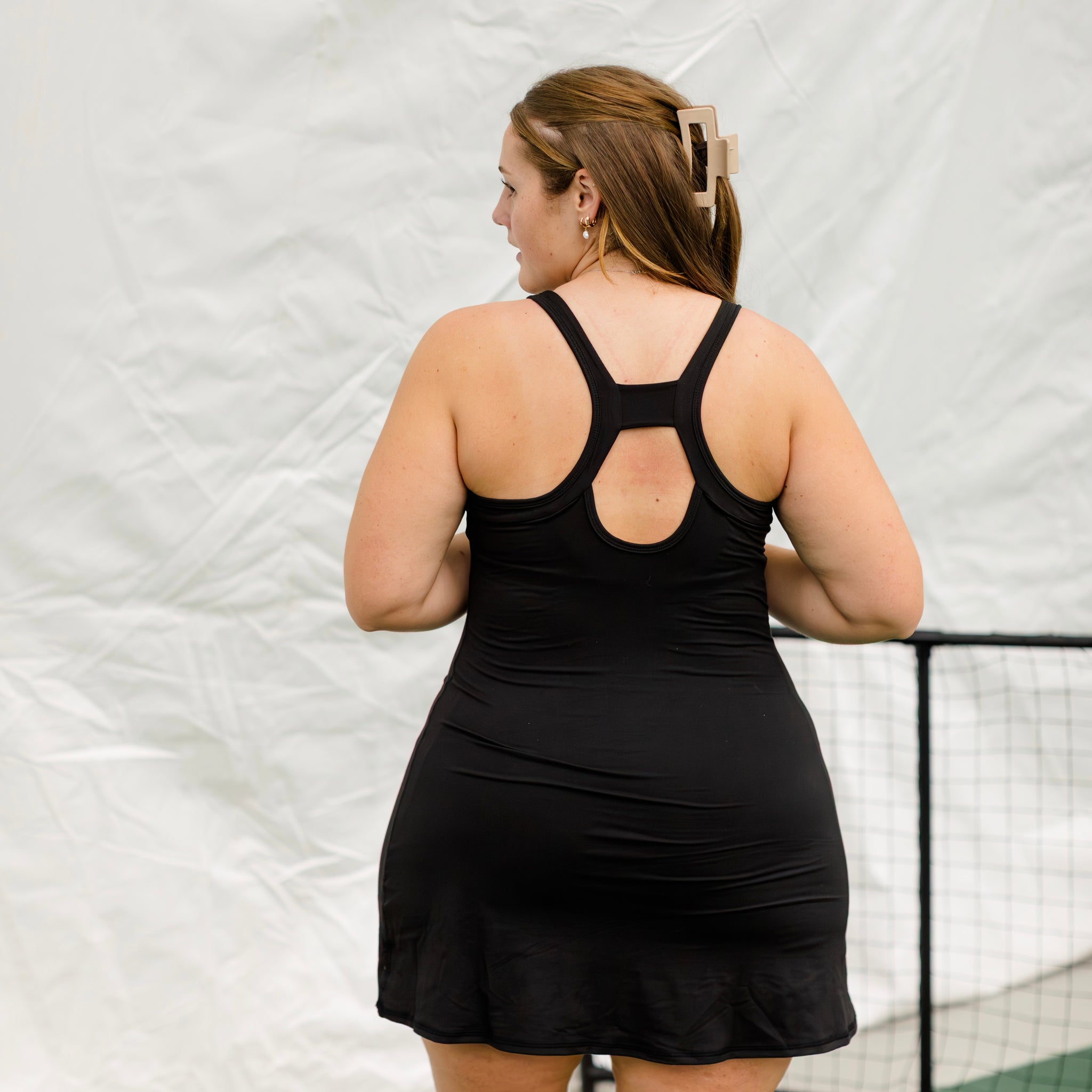Woman wearing black athletic dress on a pickleball court. Showing the back keyhole detail on the dress up close.