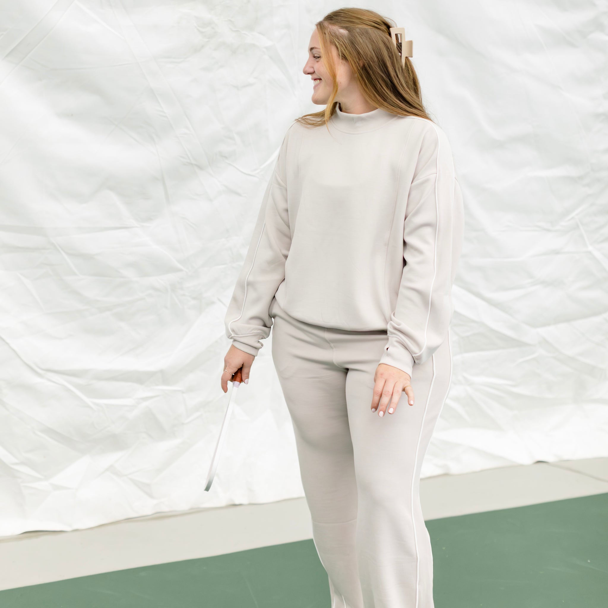 Woman wearing a beige track suit with white piping on the side. 