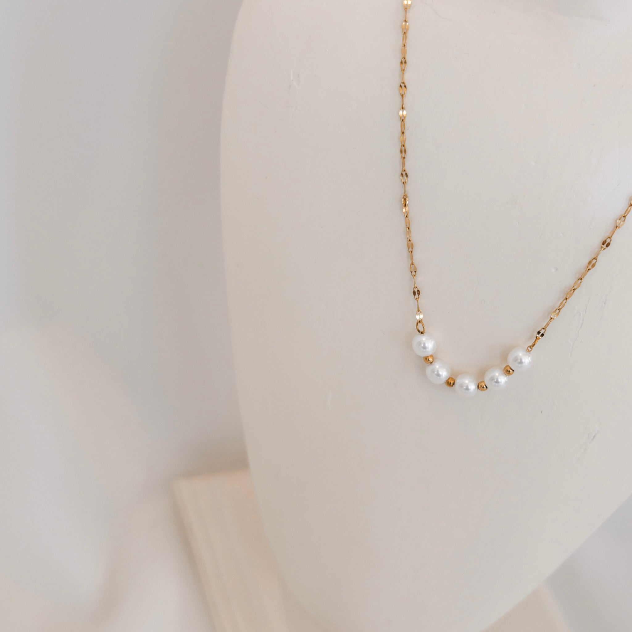 Gold necklace with pearls on a mannequin bust against a plain background