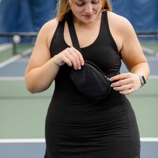 Woman opening a black crossbody bag with zipper. 