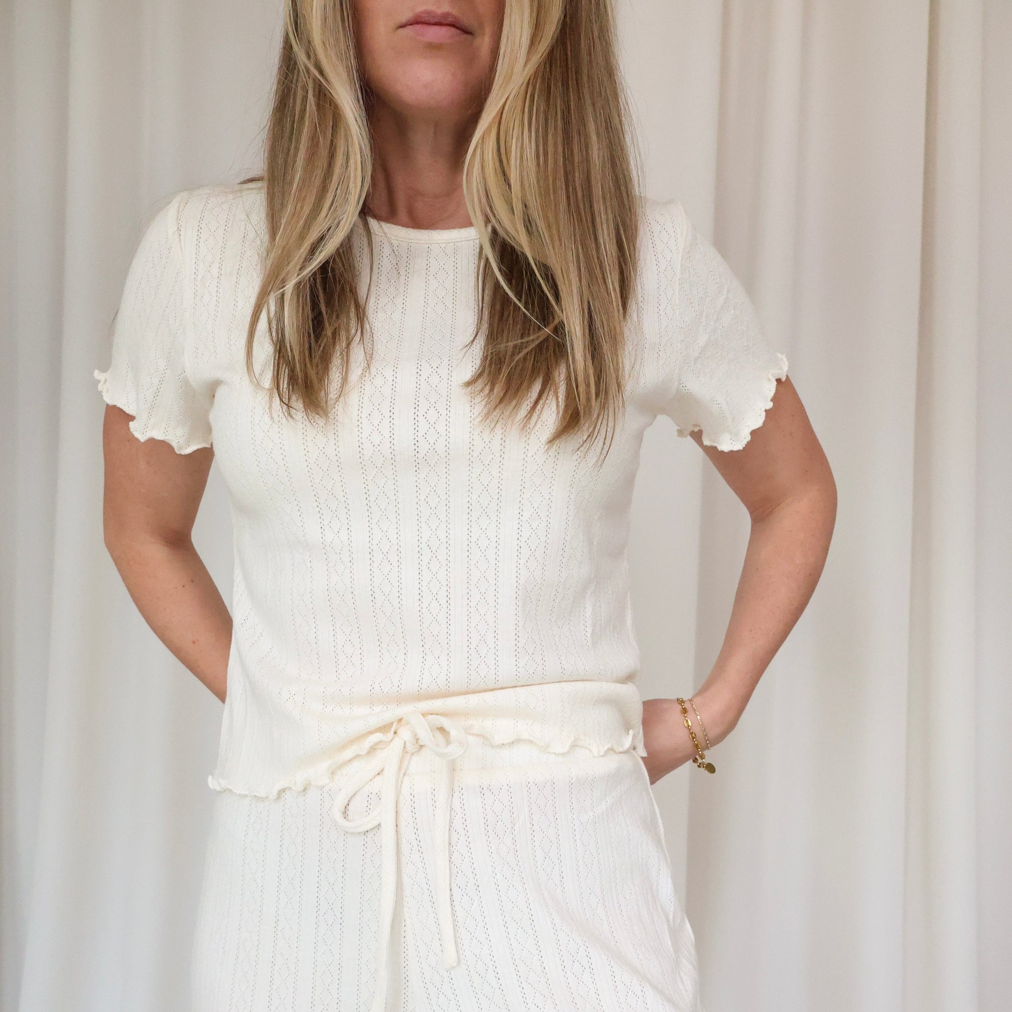 Woman wearing a white dress with ruffled sleeves against a plain background