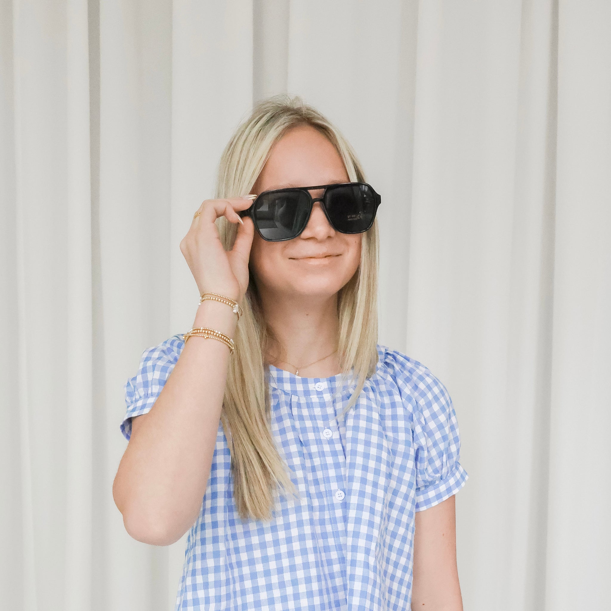 Woman wearing a blue and white checkered shirt with sunglasses against a light background