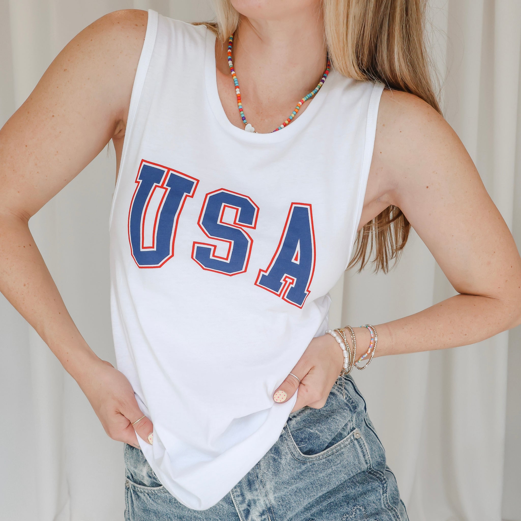 Person wearing a white tank top with 'USA' printed in blue letters against a plain background