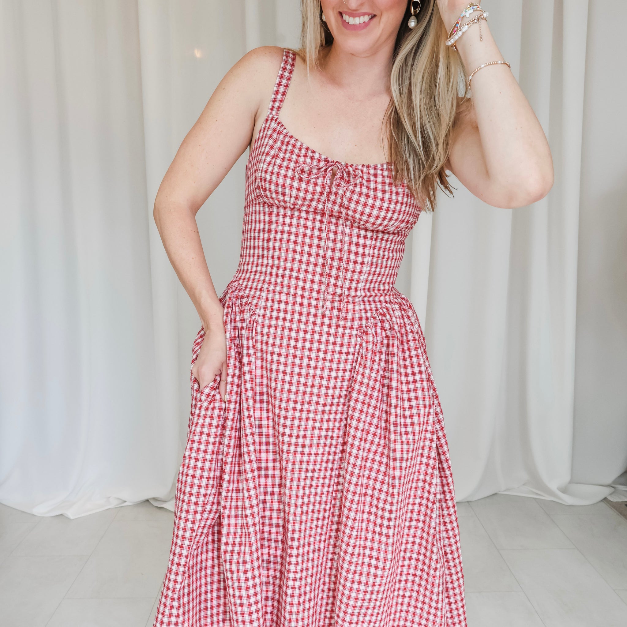 Woman wearing a red and white checkered dress against a white curtain background
