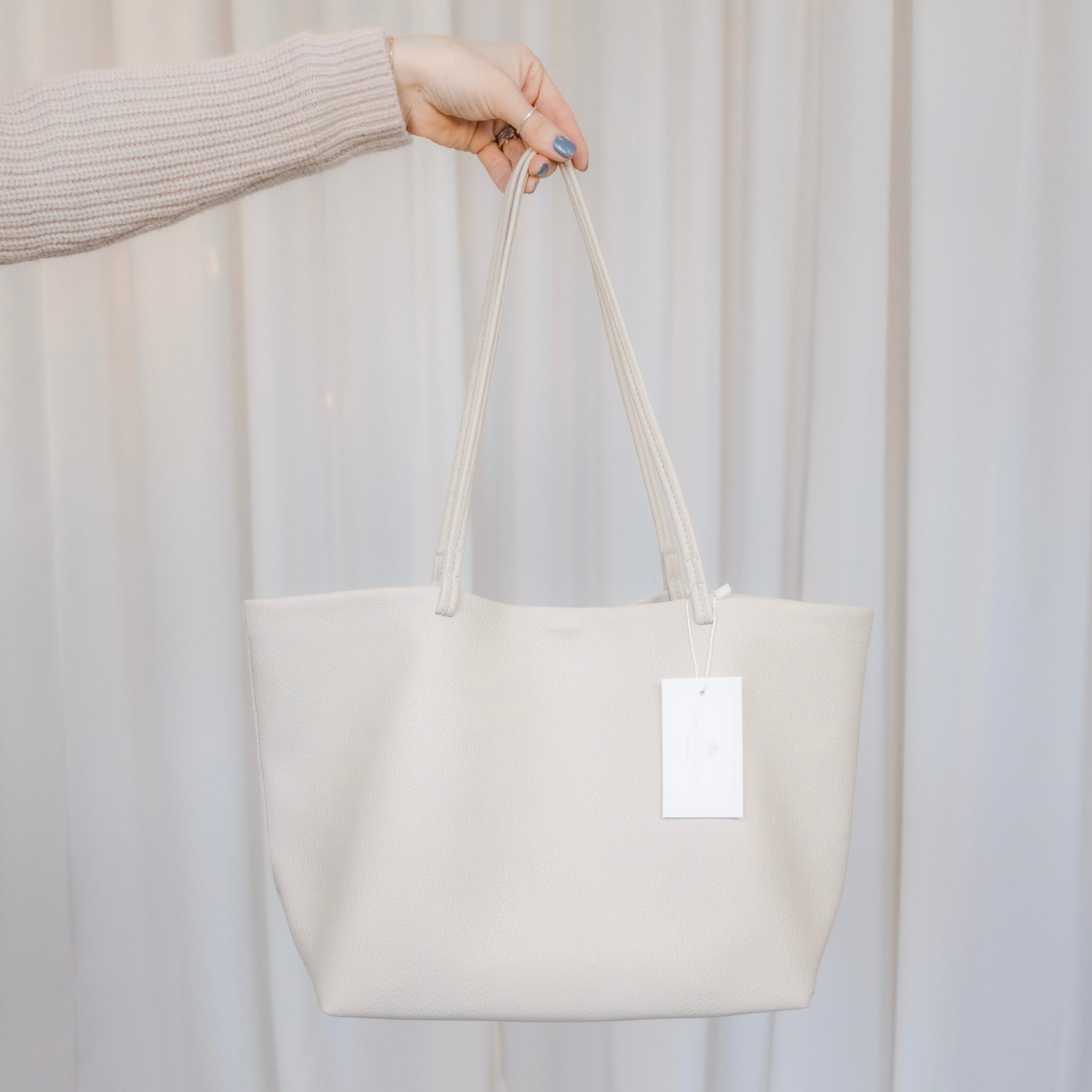 White tote bag held by a person against a plain background
