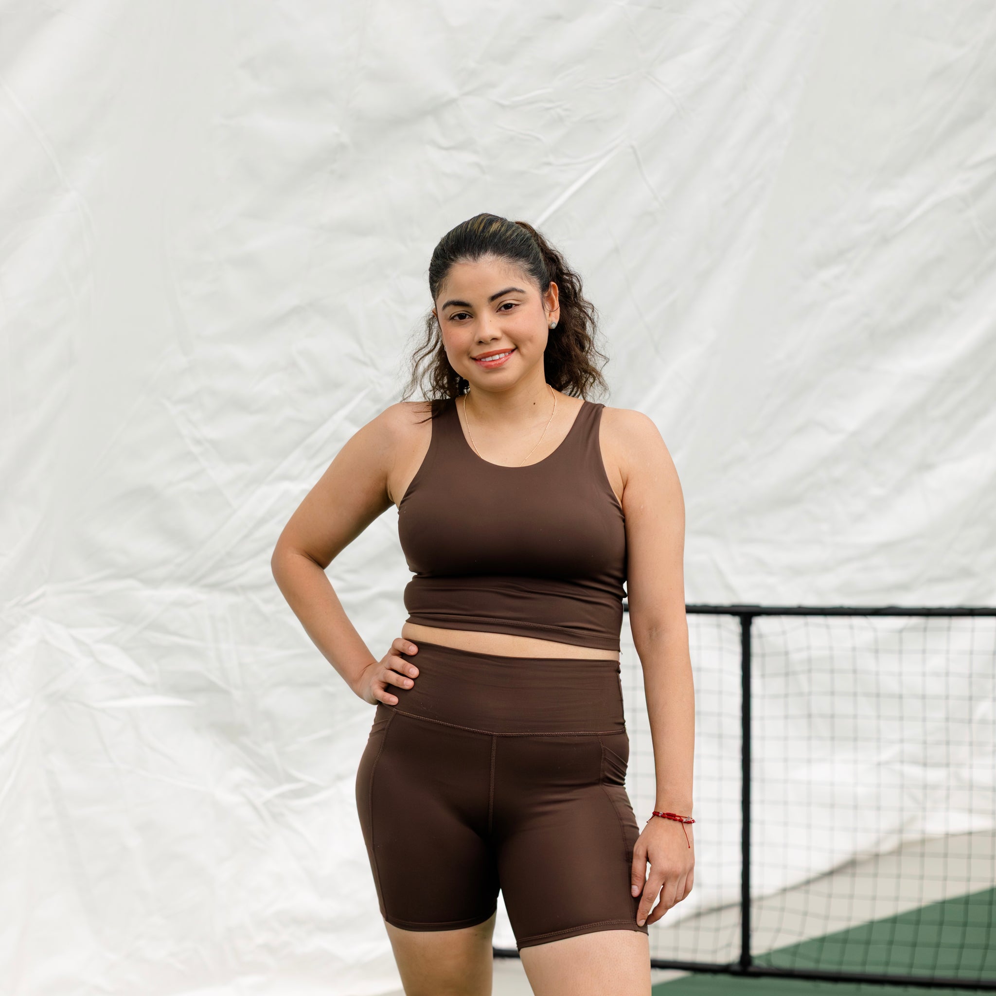 Woman wearing espresso colored athletic set with hand on hip.