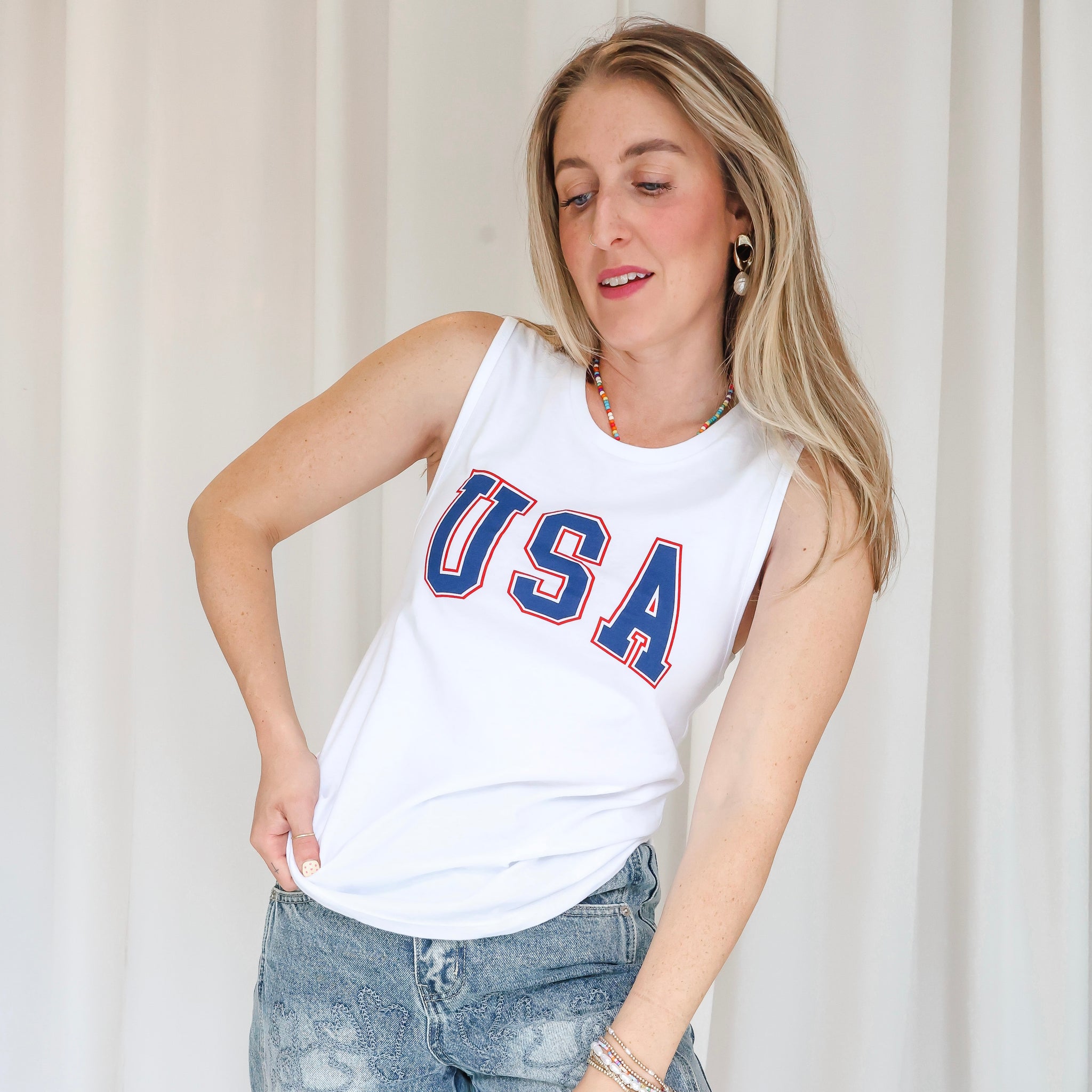 Woman wearing a white tank top with 'USA' printed on it against a plain background