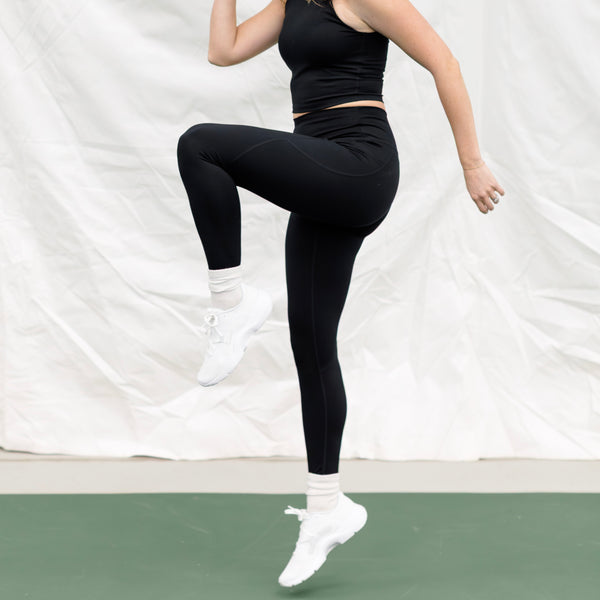 Woman jumping wearing a black athletic set. 