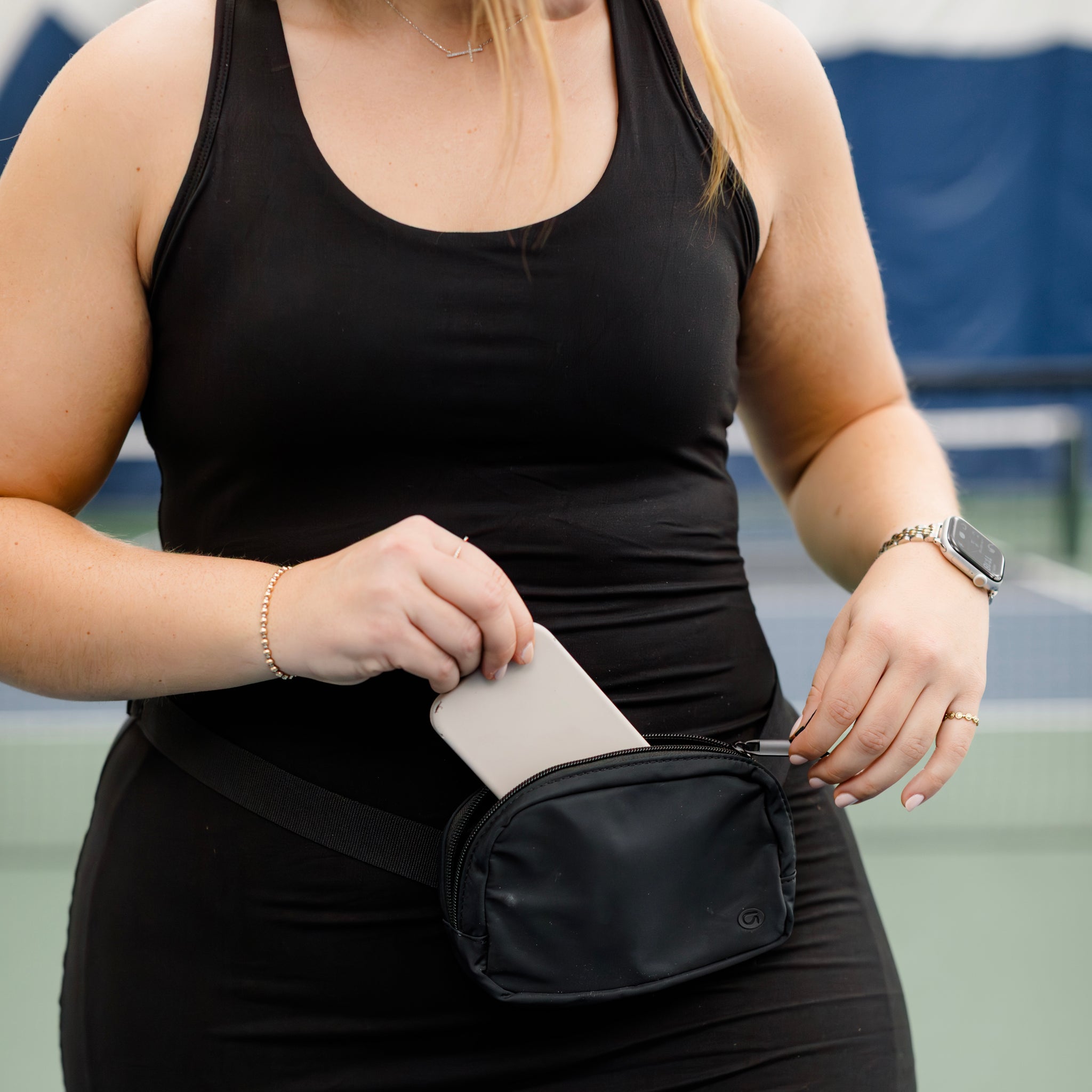 Woman putting a phone in a black crossbody bag.