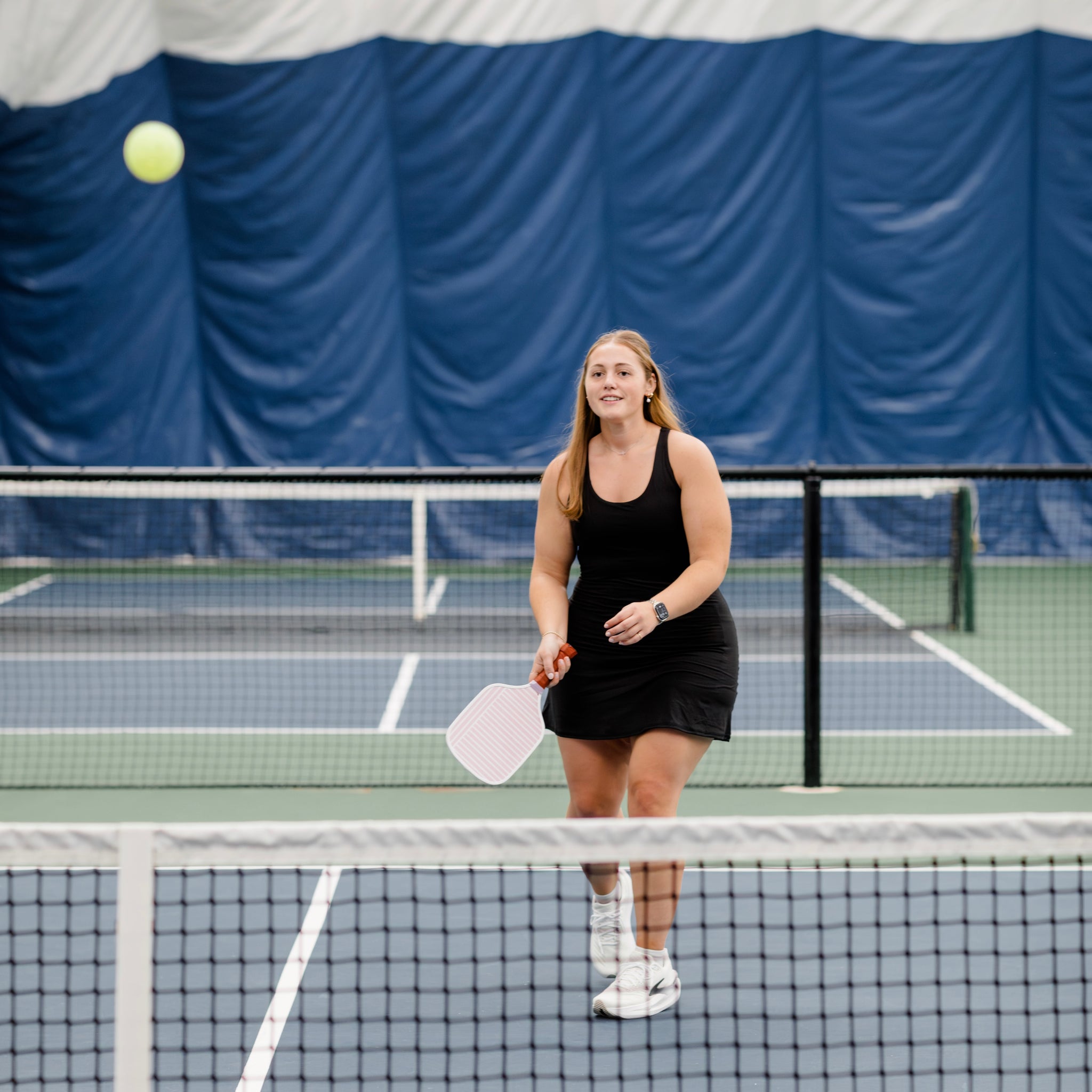 Woman wearing black athletic dress on a pickleball court while playing pickleball.