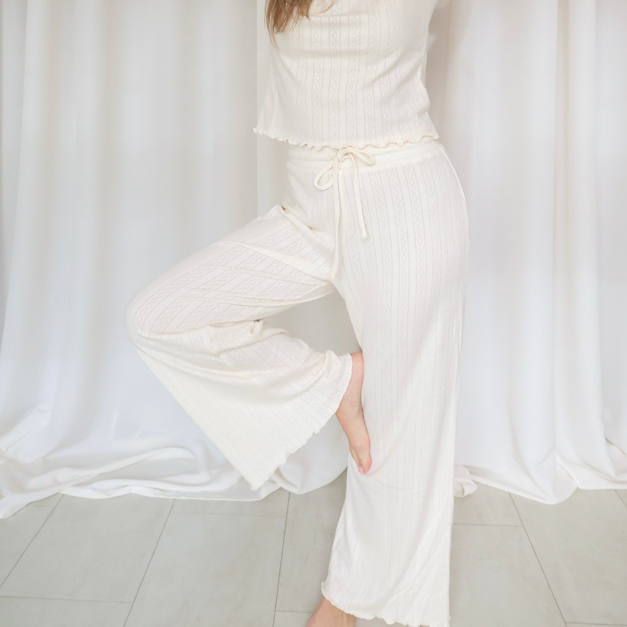 Person wearing a white outfit with a high collar and wide sleeves against a white curtain background.