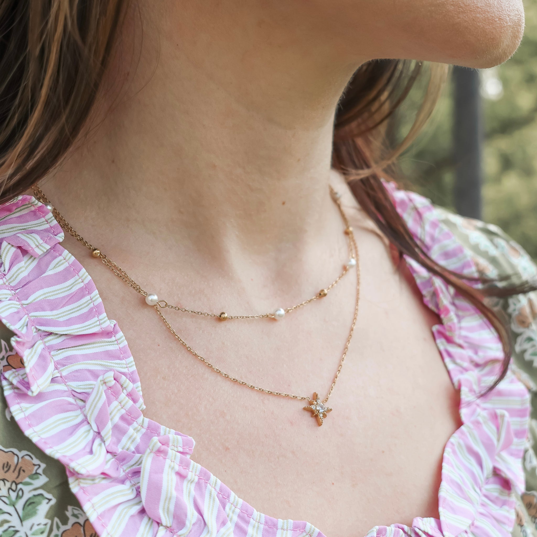 Close-up of a person wearing a delicate gold necklace with a small star pendant, outdoors.