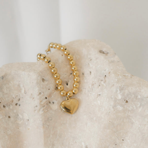 Gold beaded bracelet with a heart charm on a textured stone surface