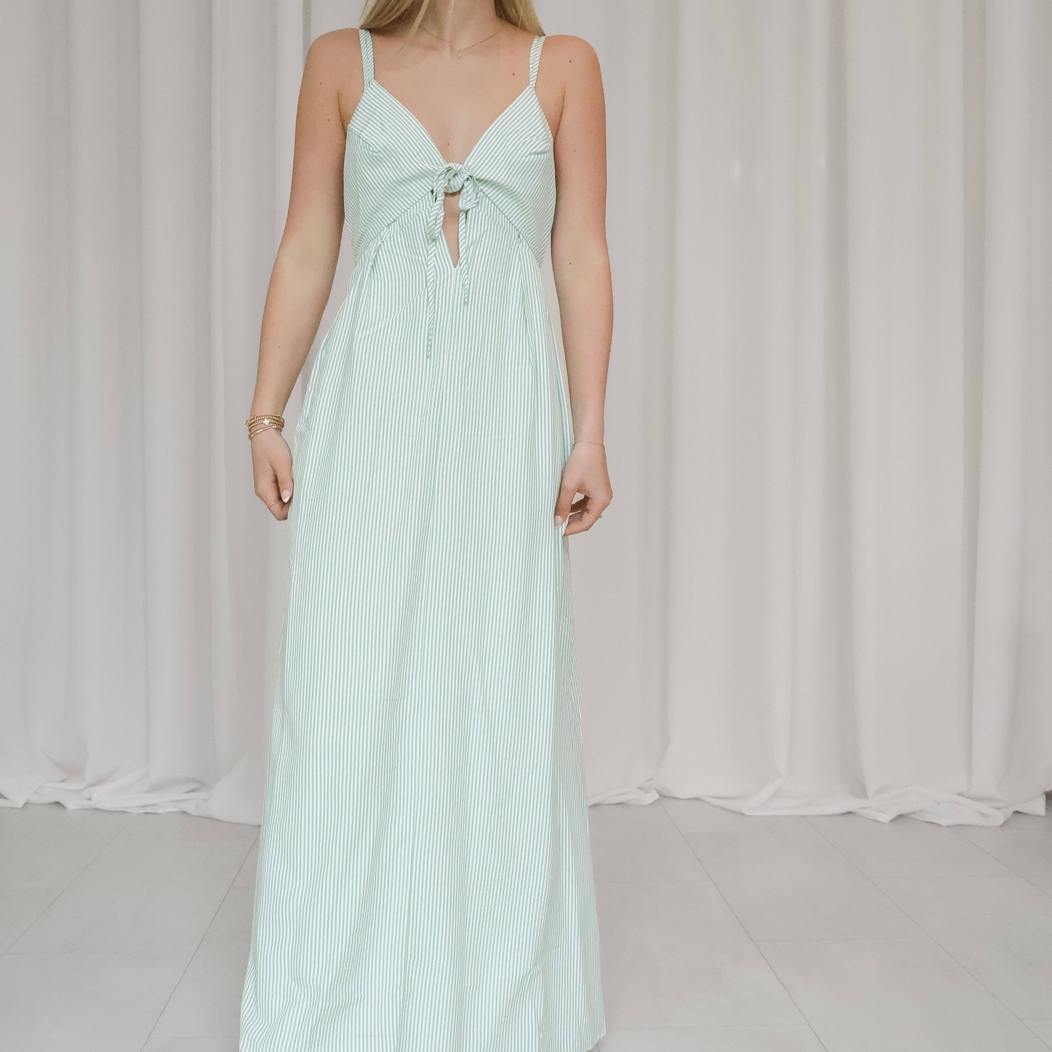 Woman wearing a light green striped dress against a white curtain background