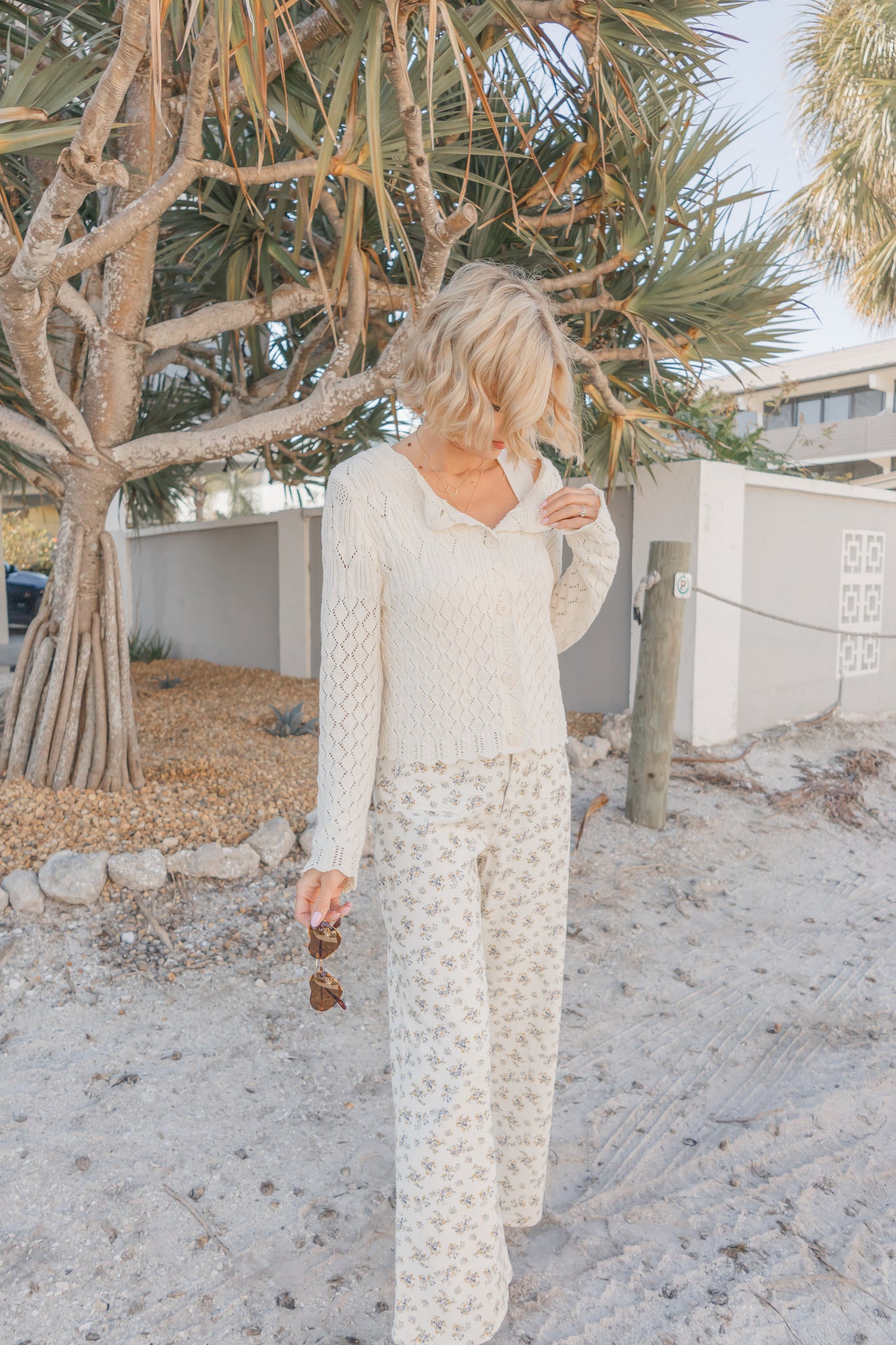 Woman in a white dress standing under a palm tree in a desert-like setting
