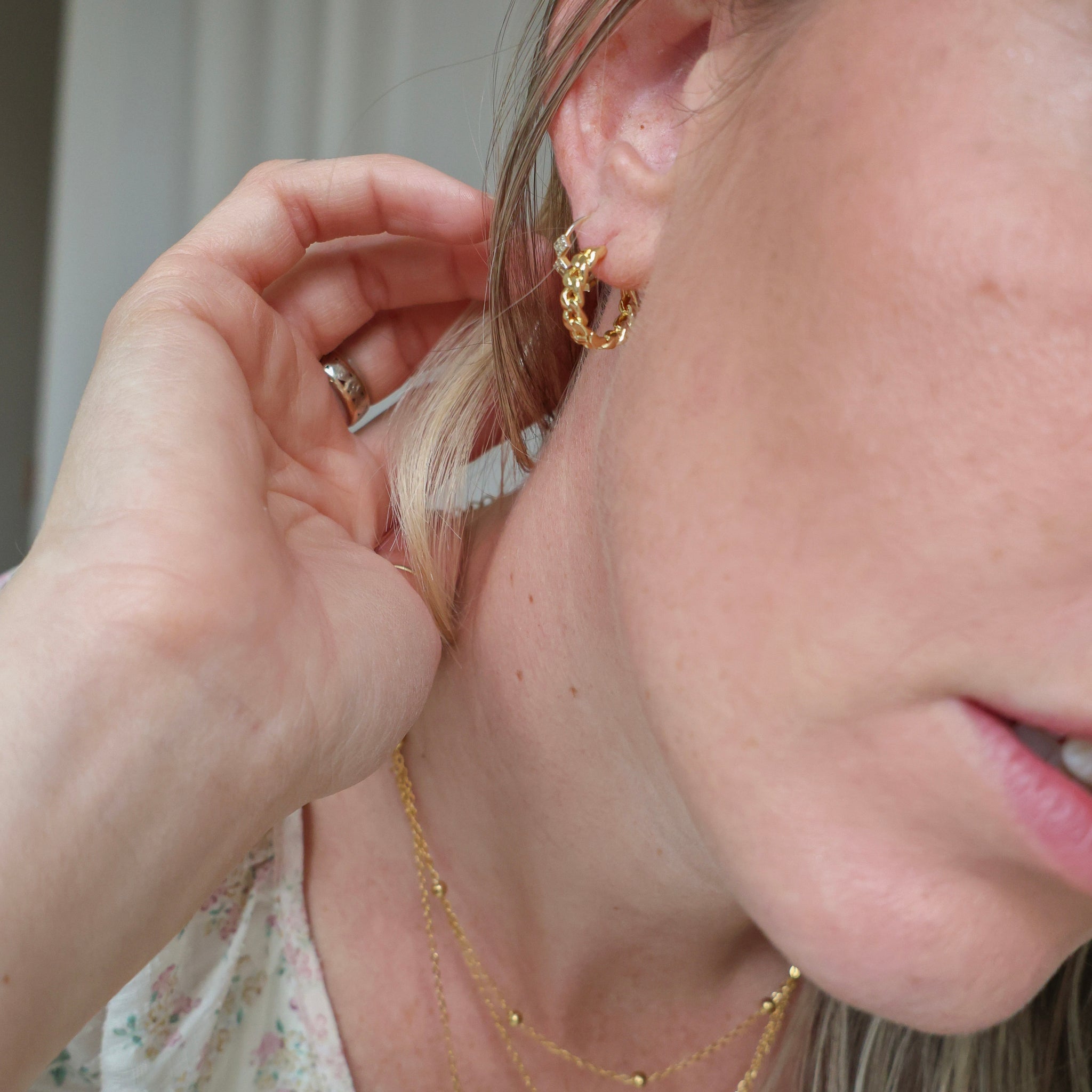 Close-up of a person wearing gold hoop earrings and a necklace.