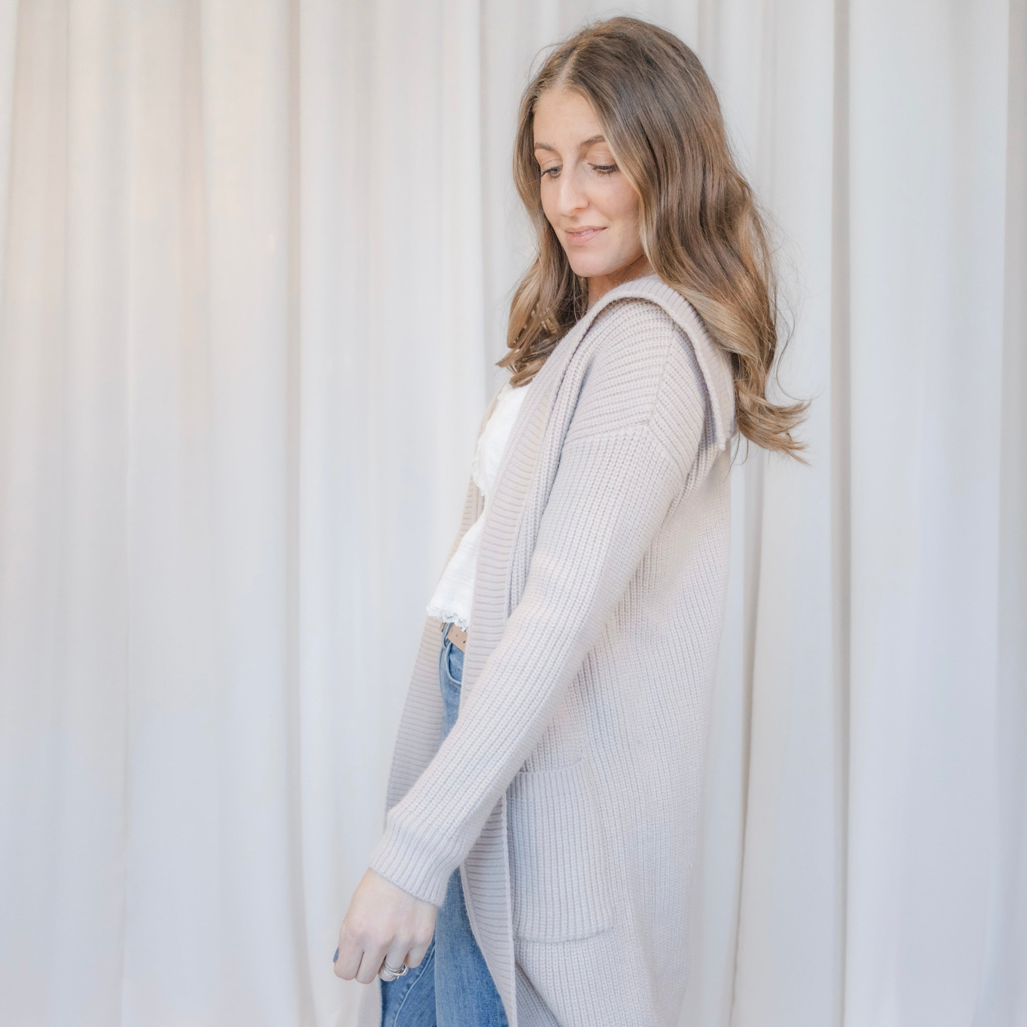Woman wearing a light gray cardigan in front of a white curtain