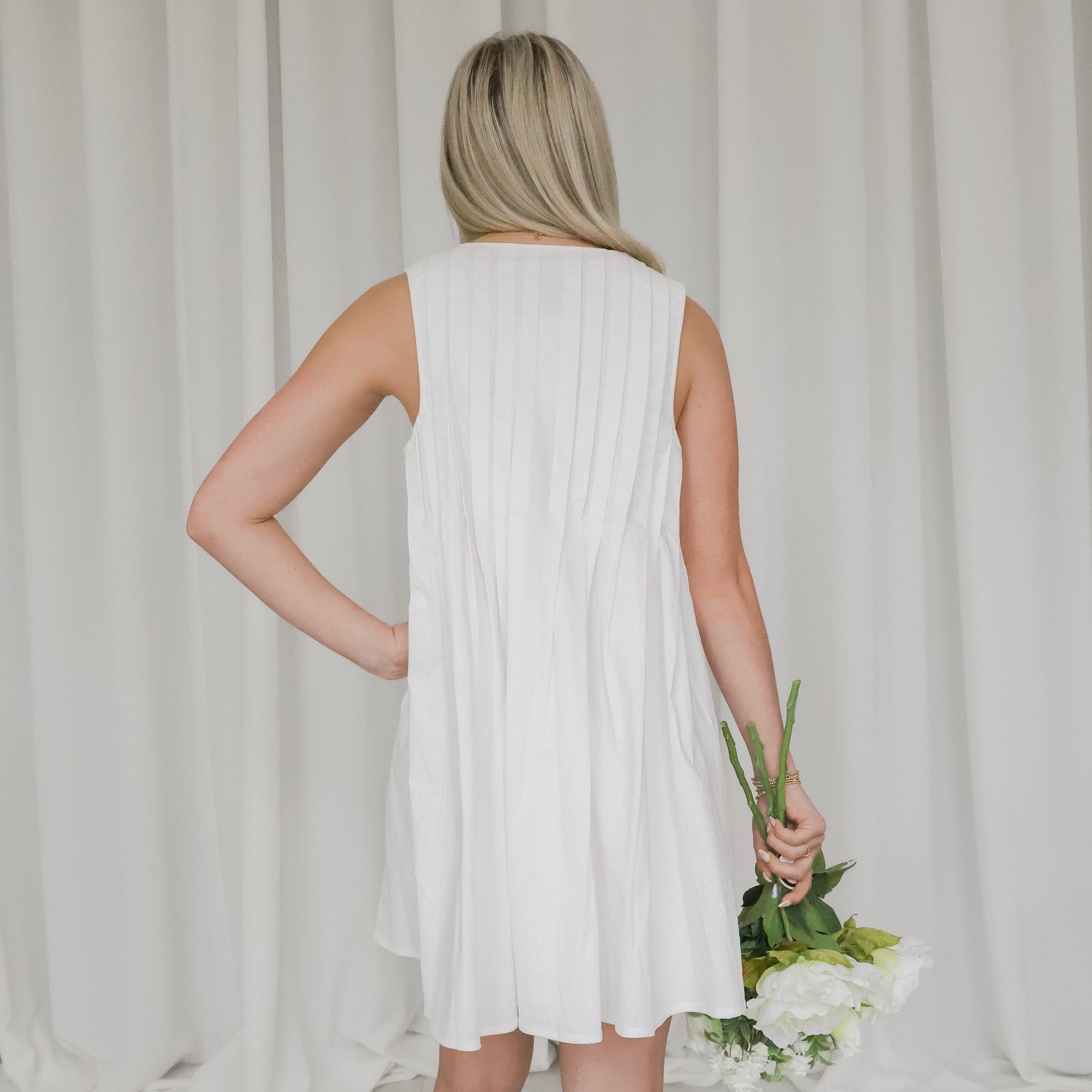 Woman in a white dress holding flowers against a plain background
