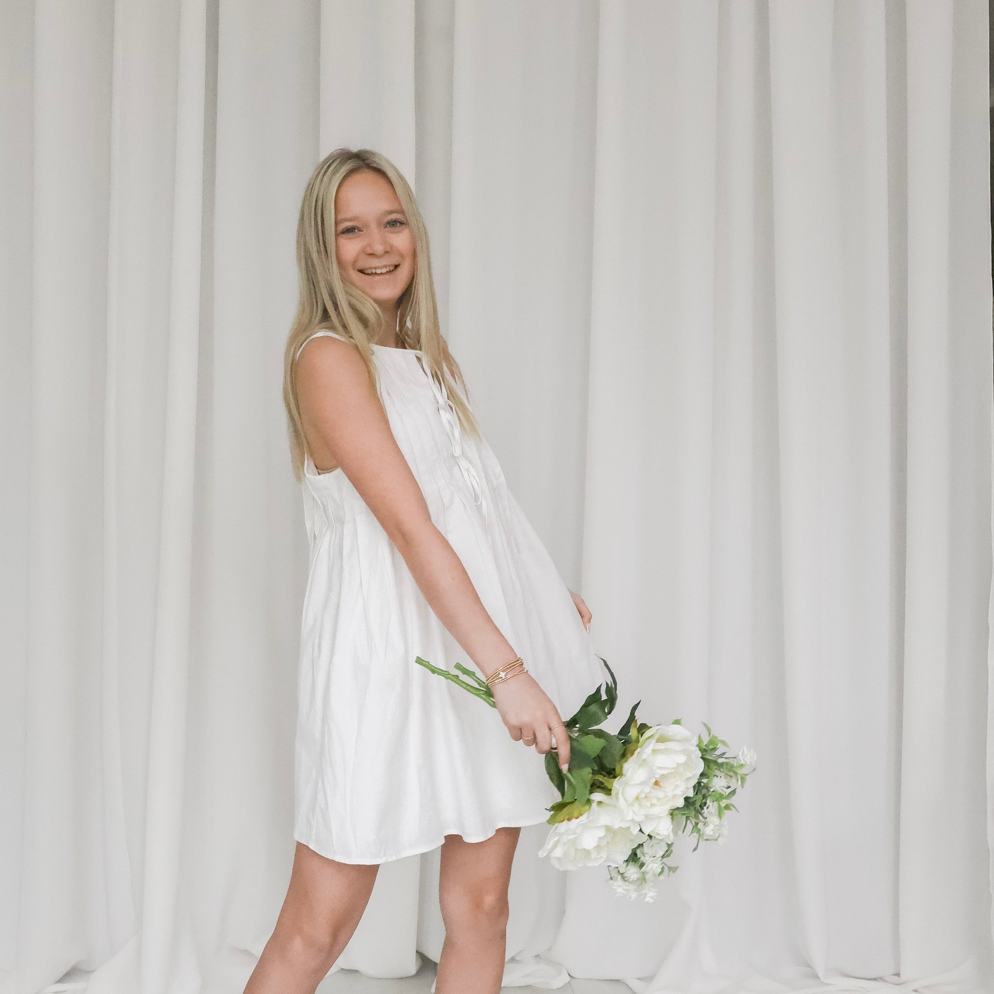 Woman in a white dress holding flowers against a plain background