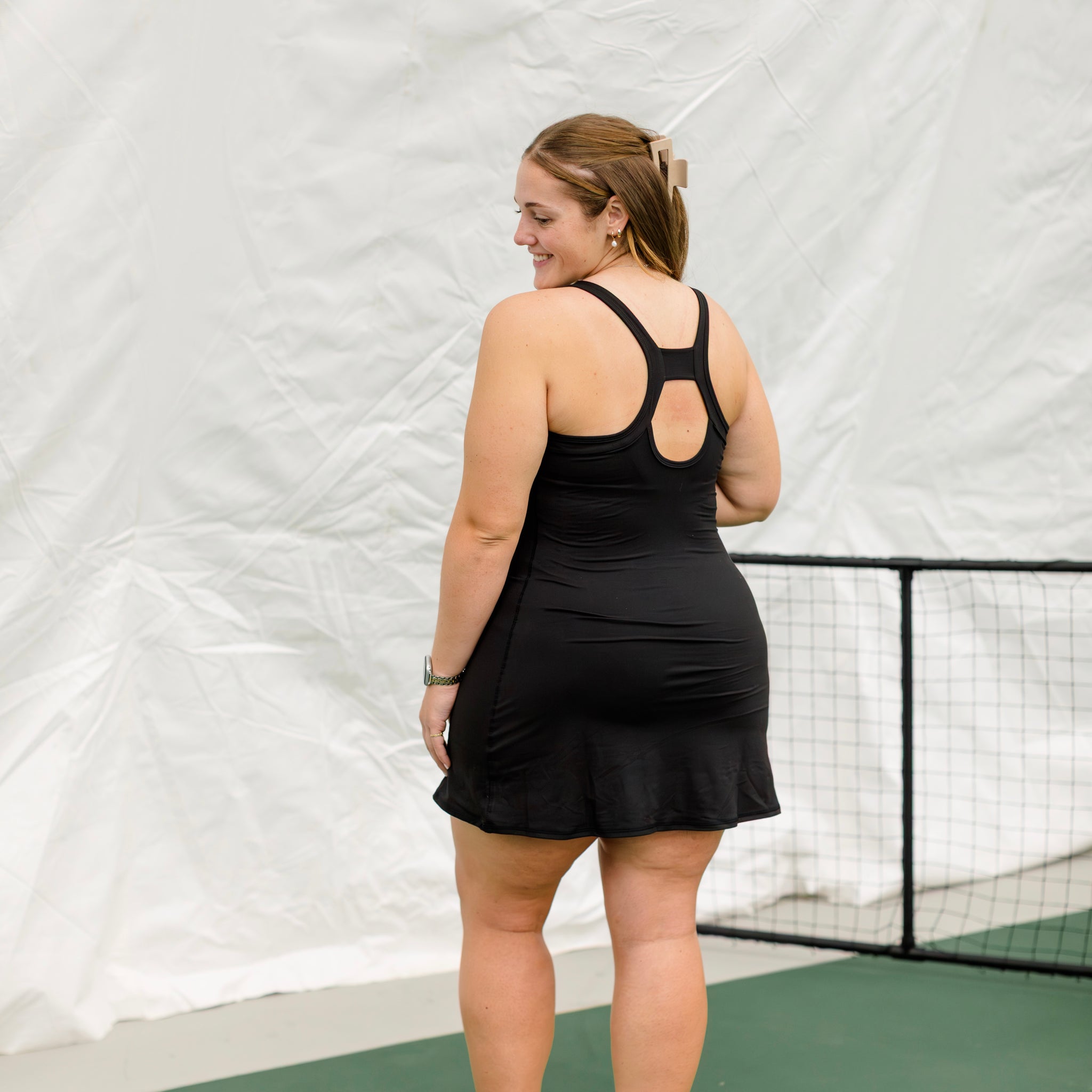 Woman wearing black athletic dress on a pickleball court. Showing the back keyhole detail on the dress.