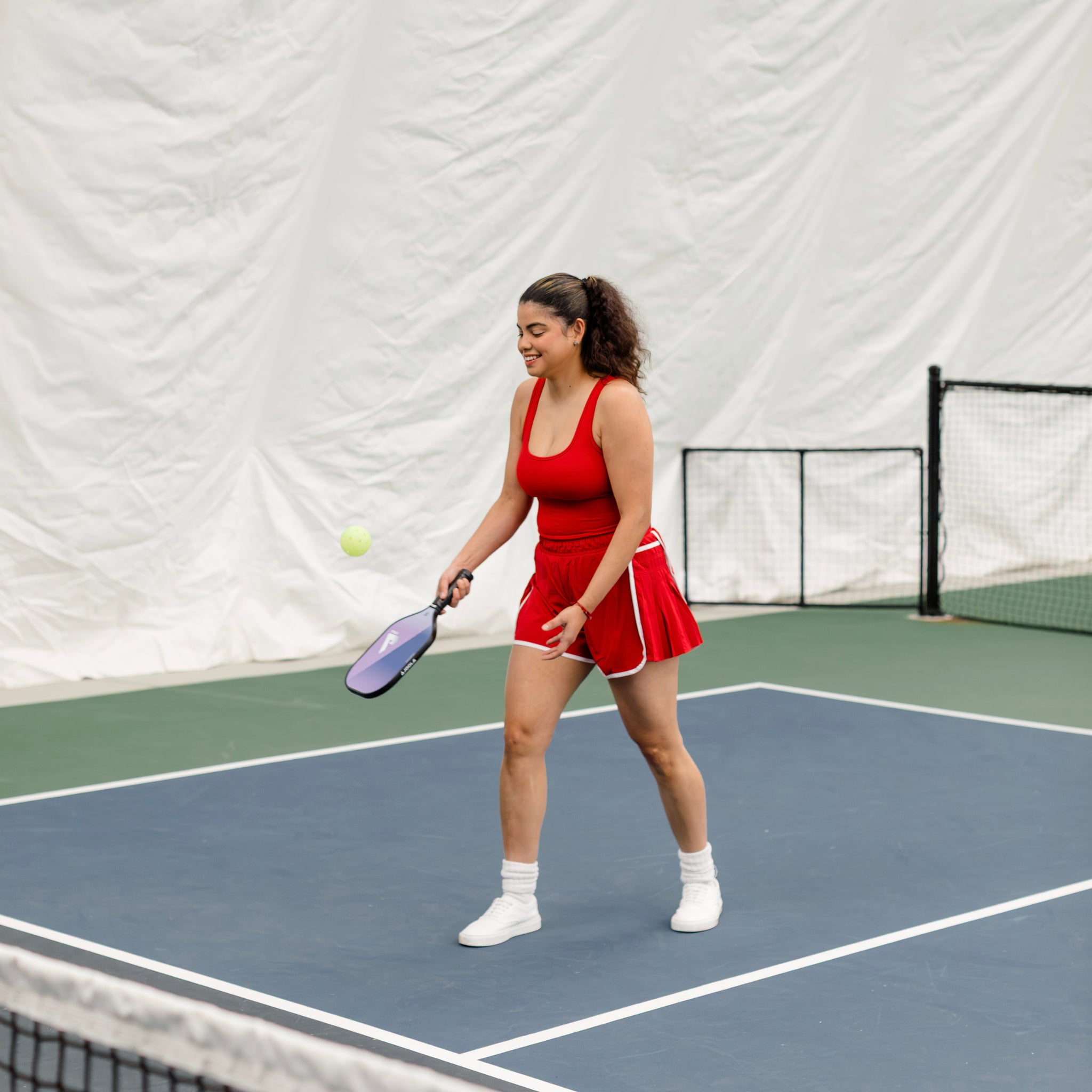 Woman wearing a red and white shortsie while playing pickleball on an indoor court.
