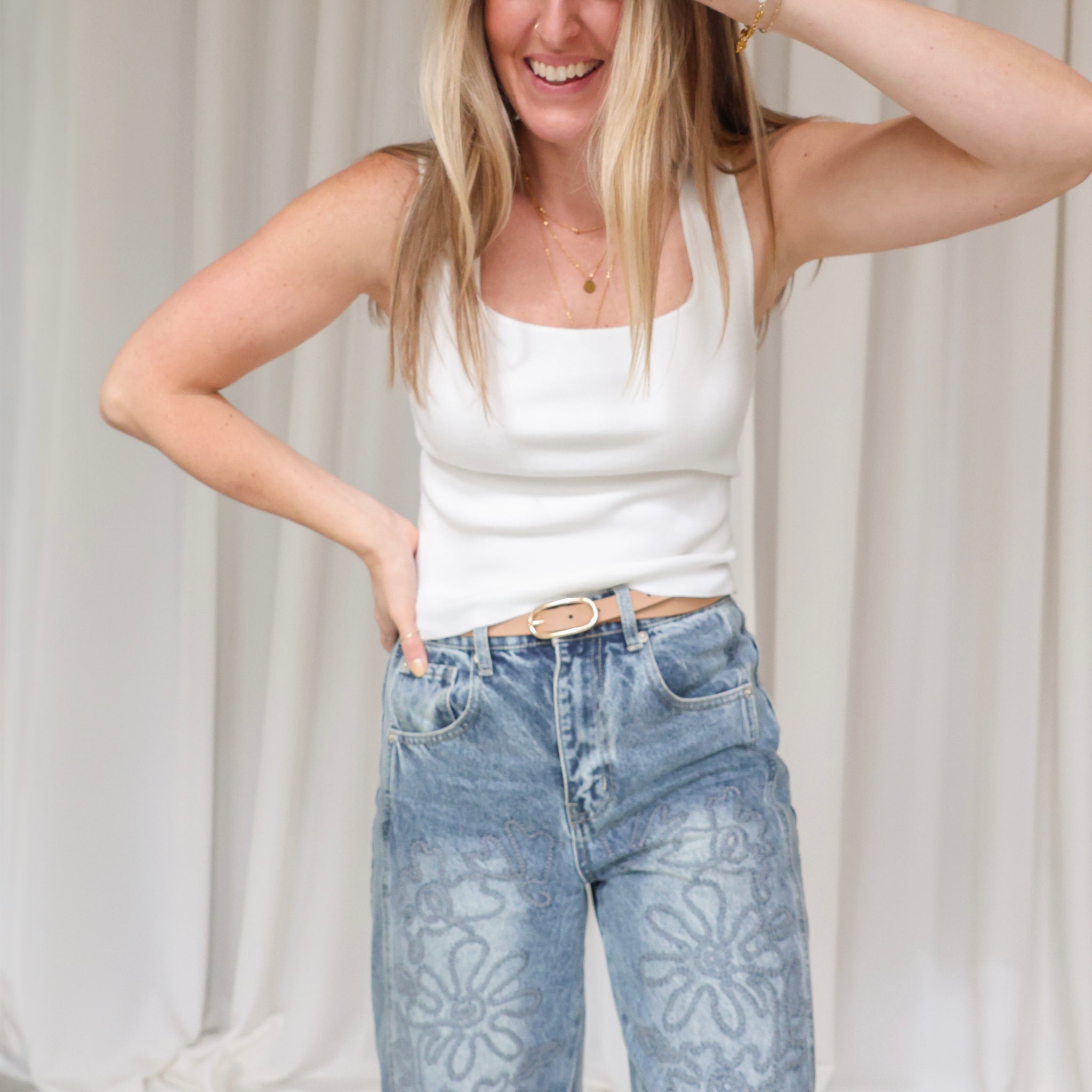 Woman wearing a white tank top and blue jeans against a plain background