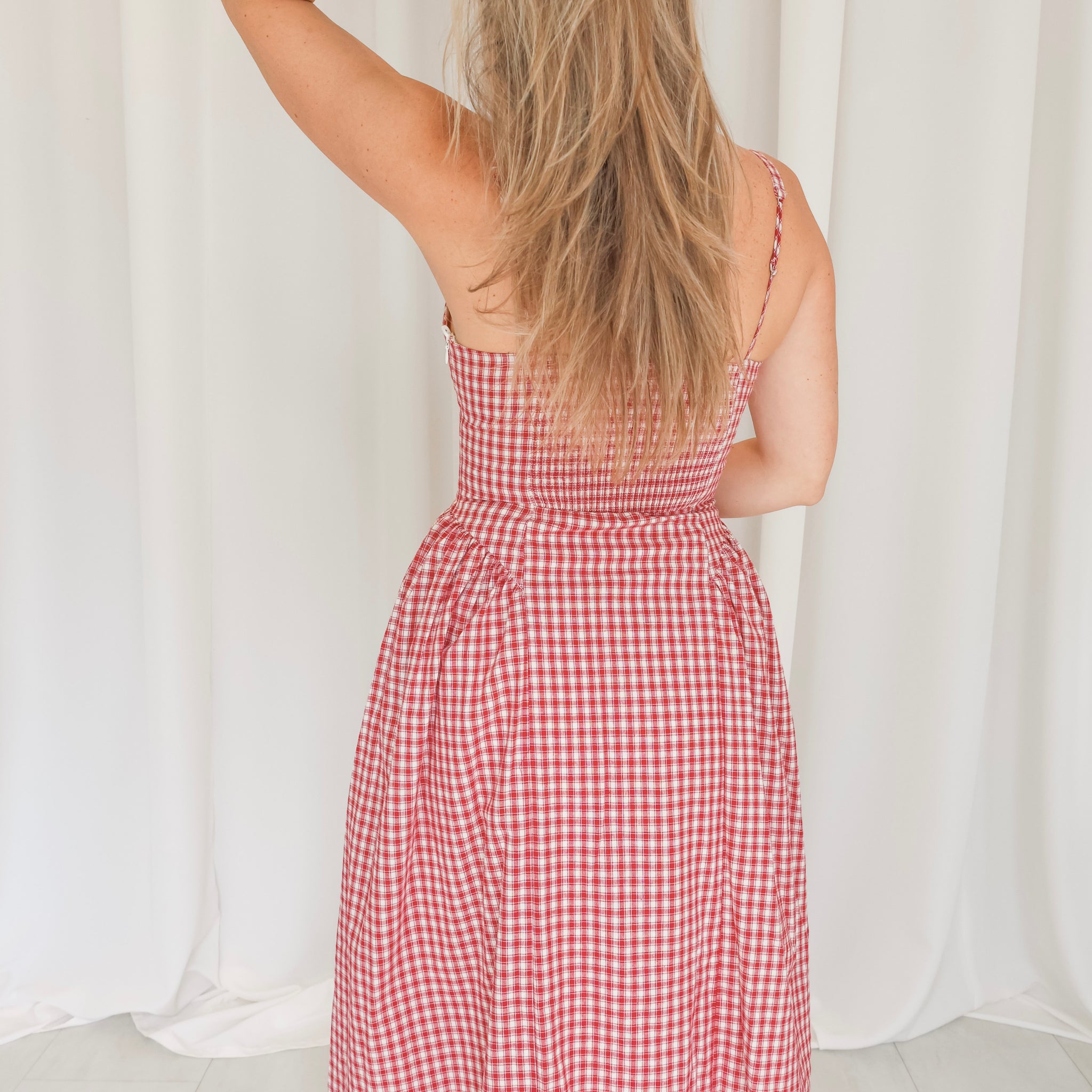 Person wearing a red and white checkered dress against a white curtain background