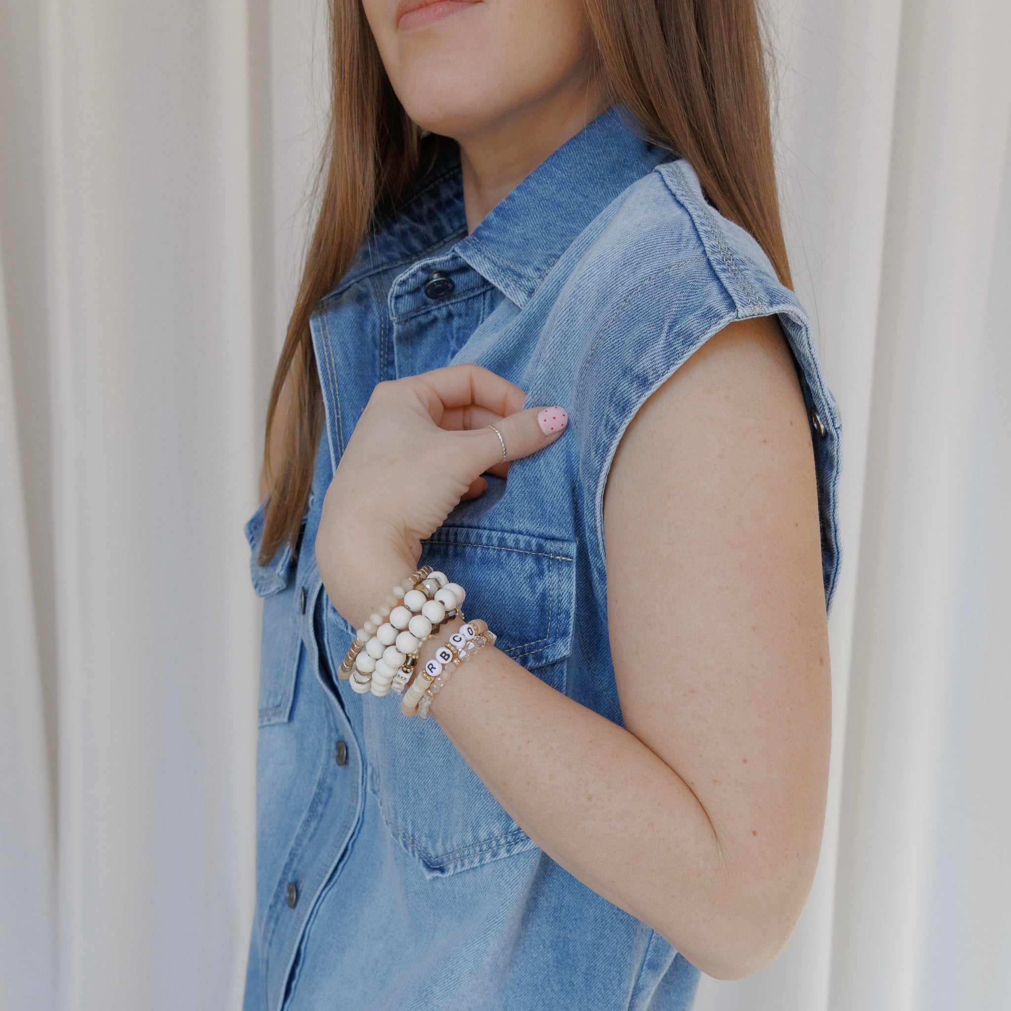 Person wearing a denim vest with visible jewelry against a neutral background