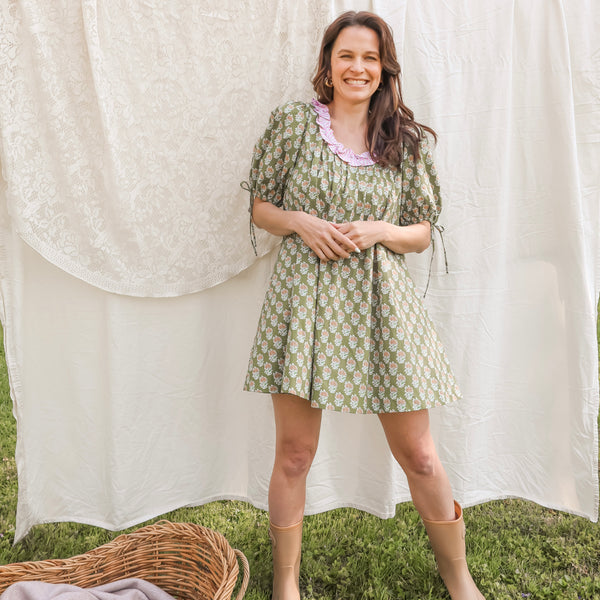 Woman in a green patterned dress standing in front of white fabric outdoors