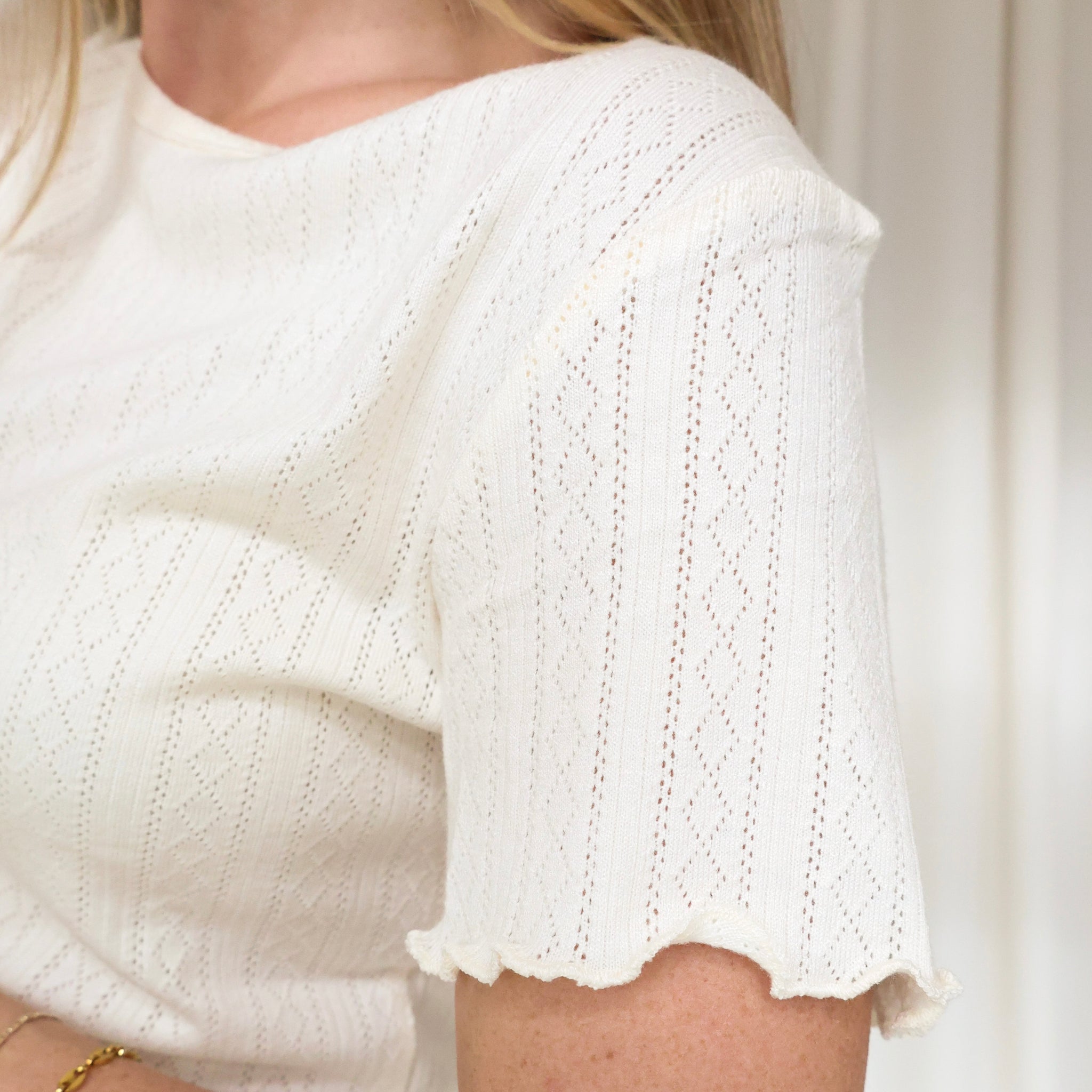 White knitted top with short sleeves on a neutral background