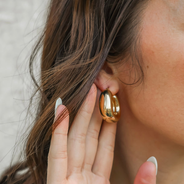 Gold hoop earring worn by a person with a neutral background
