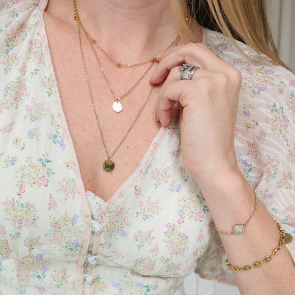 Person wearing a floral dress with gold jewelry including necklaces, rings, and a bracelet.
