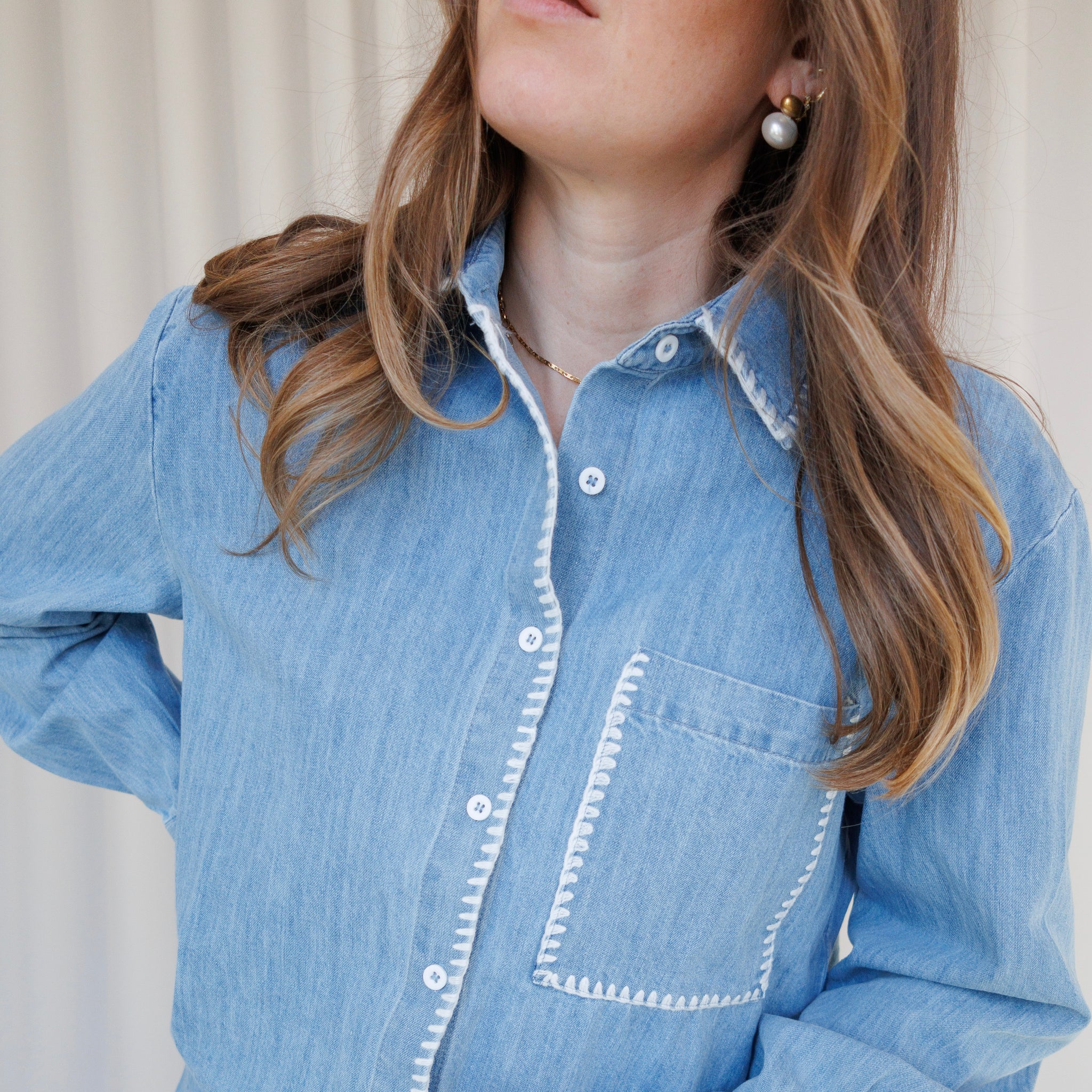 Person wearing a light blue denim shirt with white trim against a neutral background