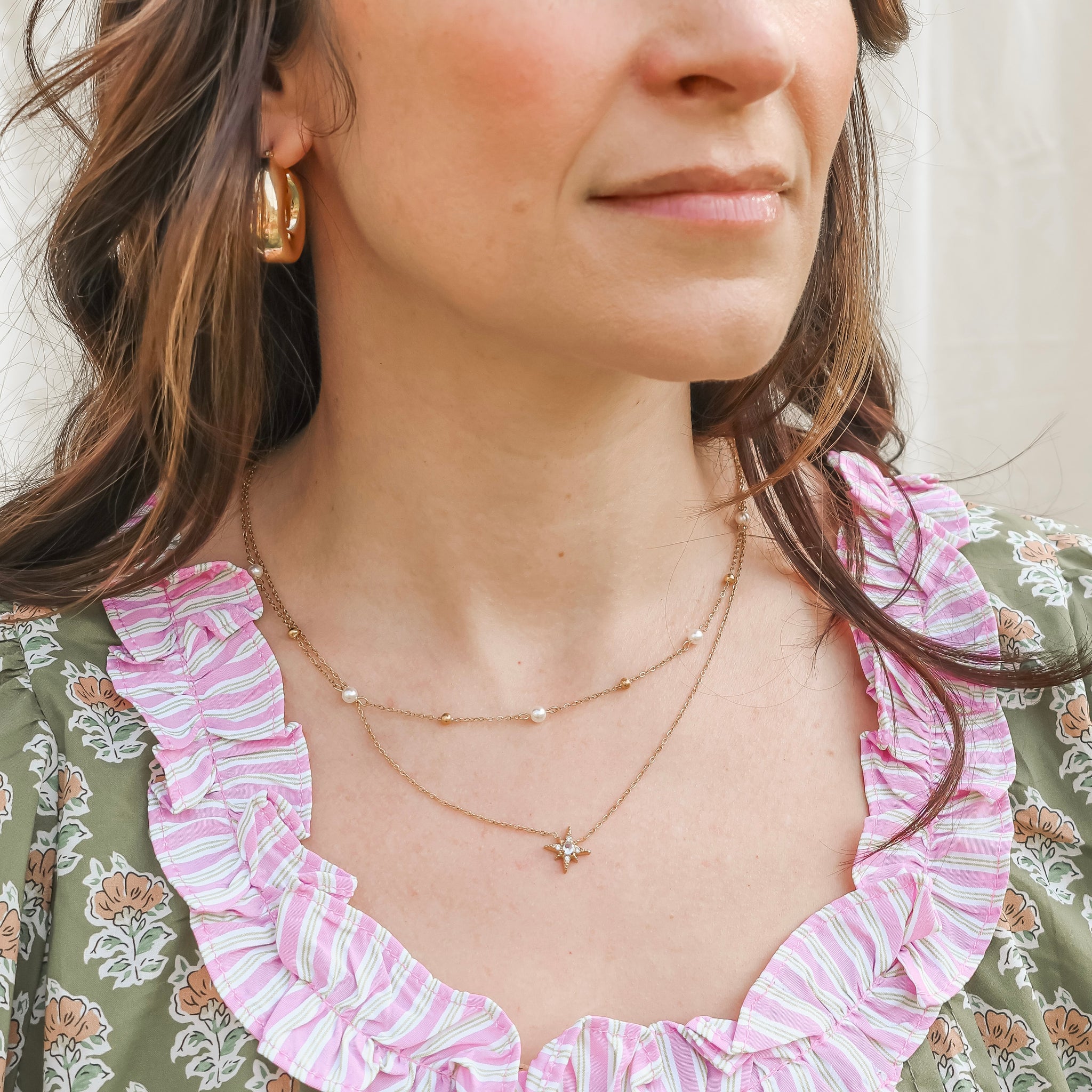 Close-up of a woman wearing a gold necklace and earrings with a floral dress.