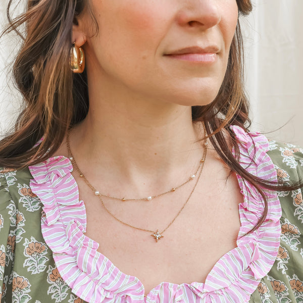Close-up of a woman wearing a gold necklace and earrings with a floral dress.