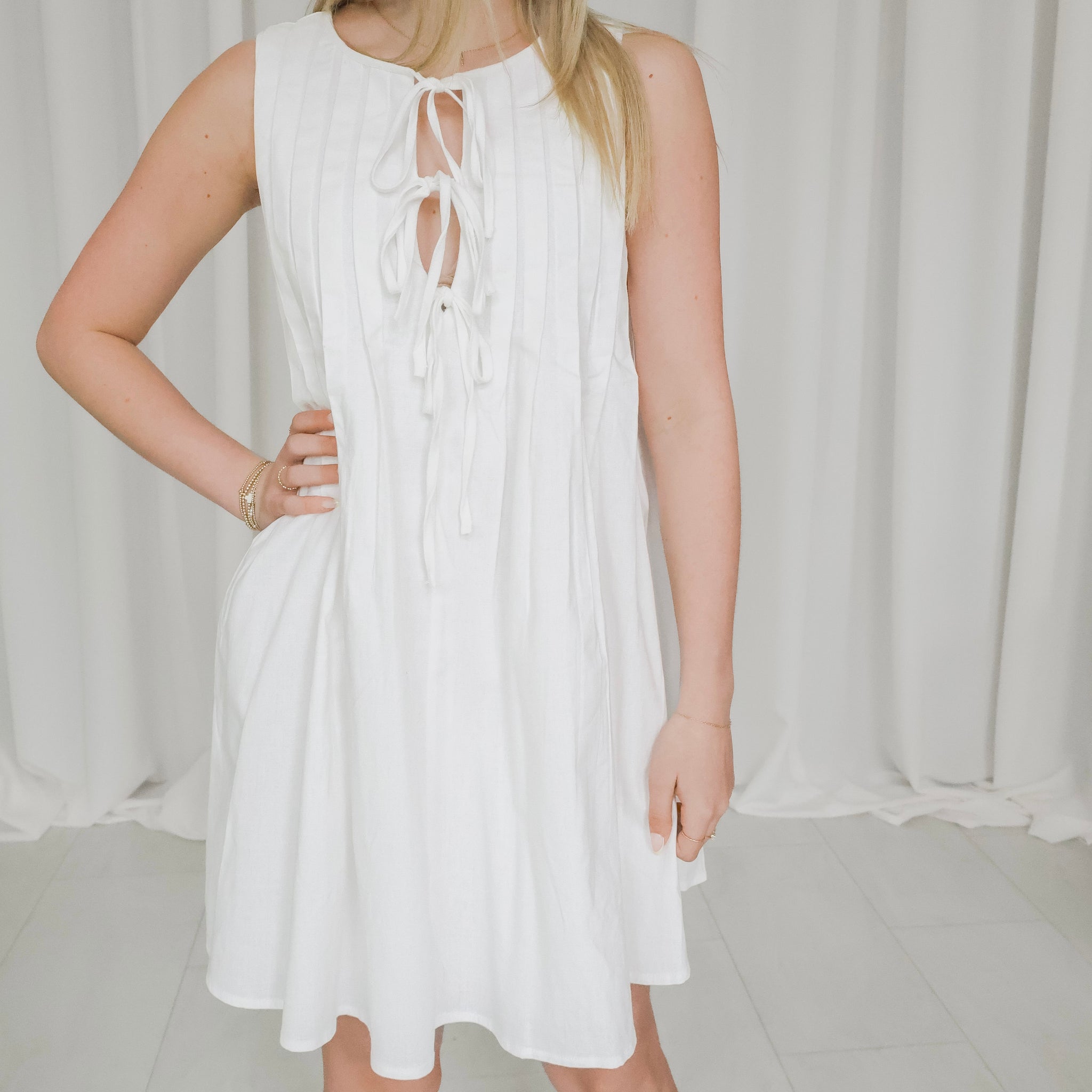 White sleeveless dress with lace-up front worn by a person against a white curtain background