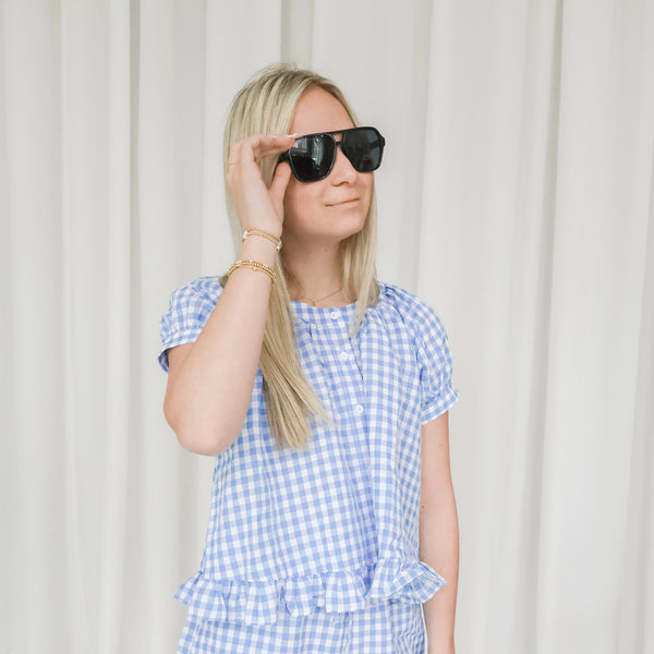 Woman wearing a blue and white checkered outfit with sunglasses against a plain background
