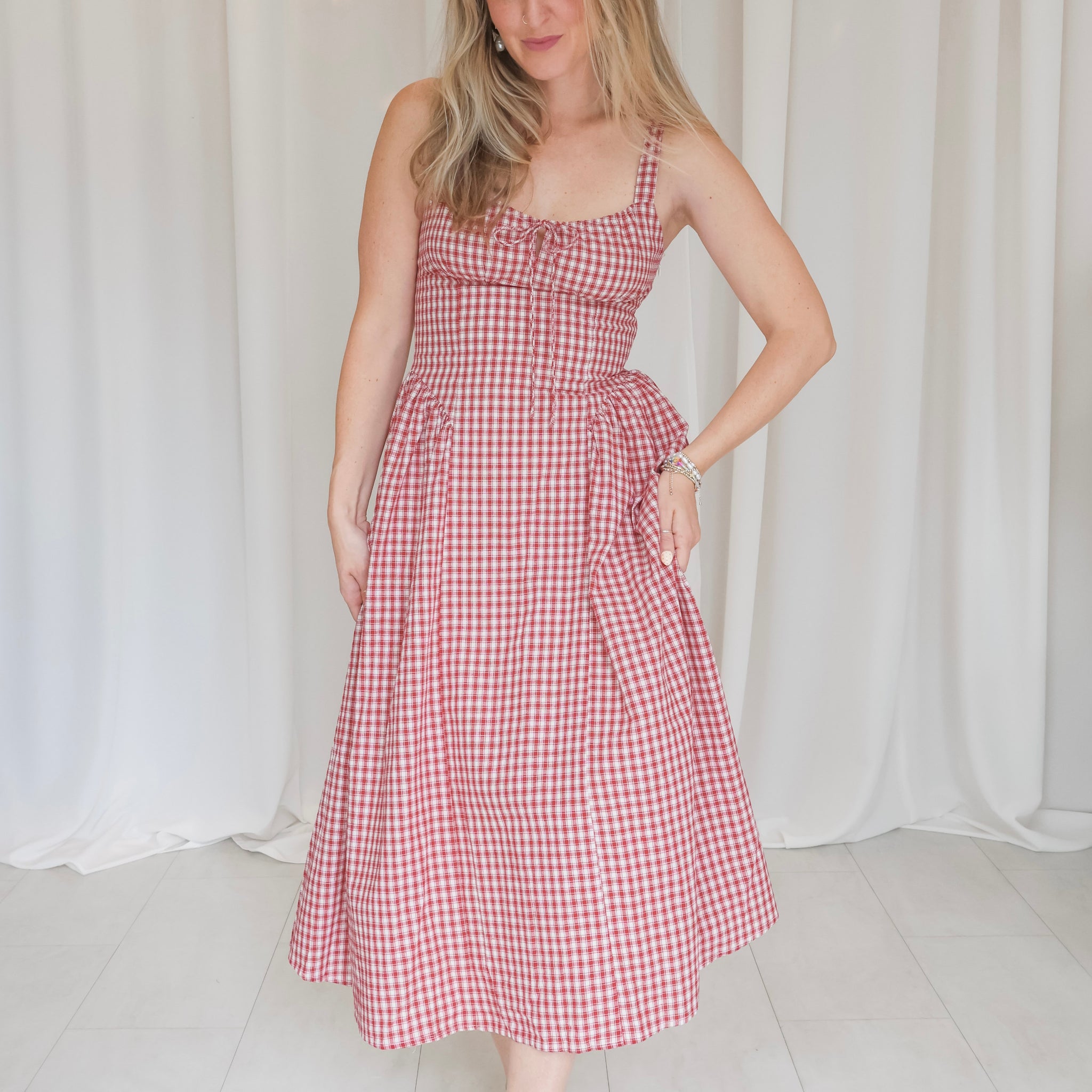 Woman wearing a red and white checkered dress against a white curtain background