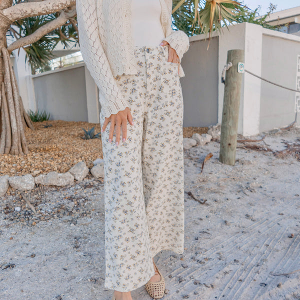 Person wearing a white knit sweater and floral pants standing outdoors.
