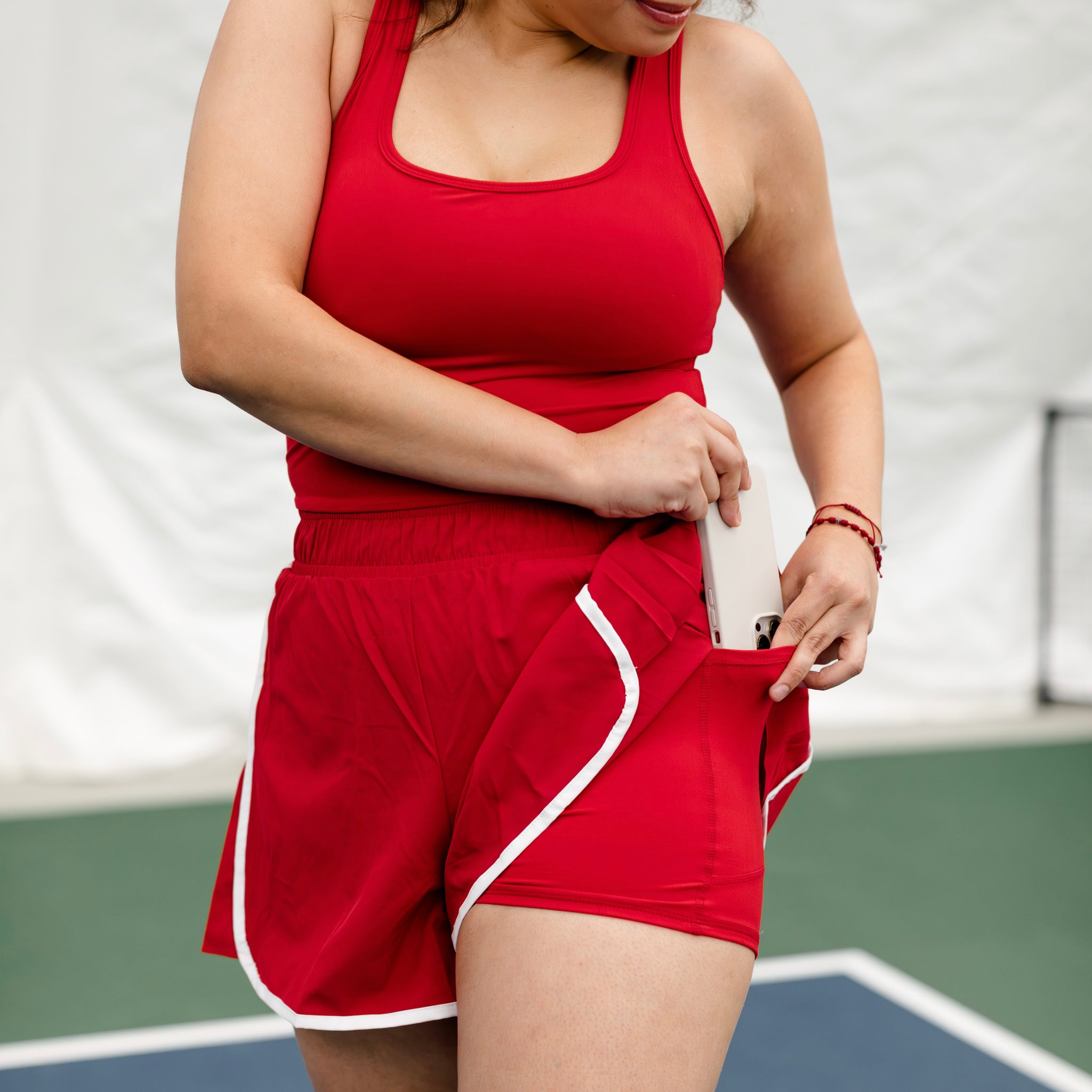 Woman wearing a red and white shortsie and showing how to put a phone in the pocket that is on the shorts. 