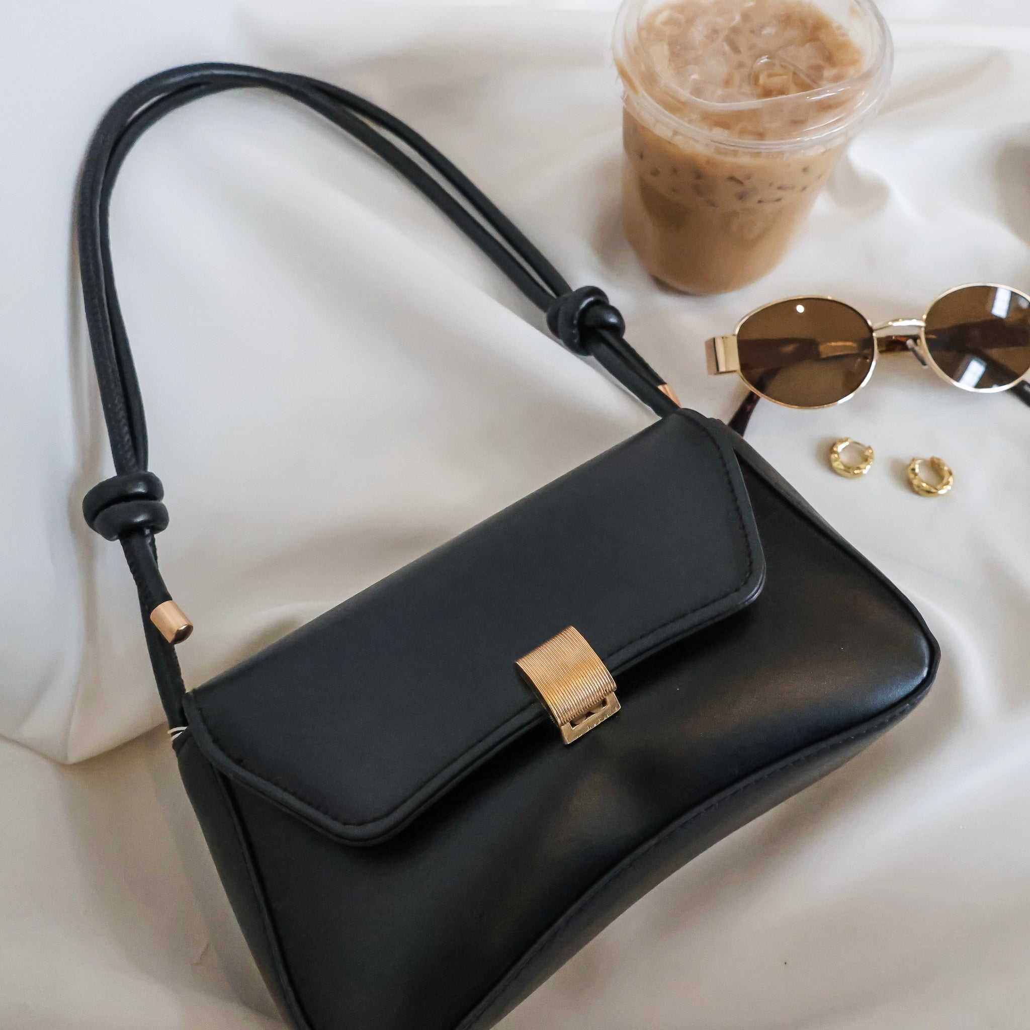 Black handbag with sunglasses and a drink on a white surface