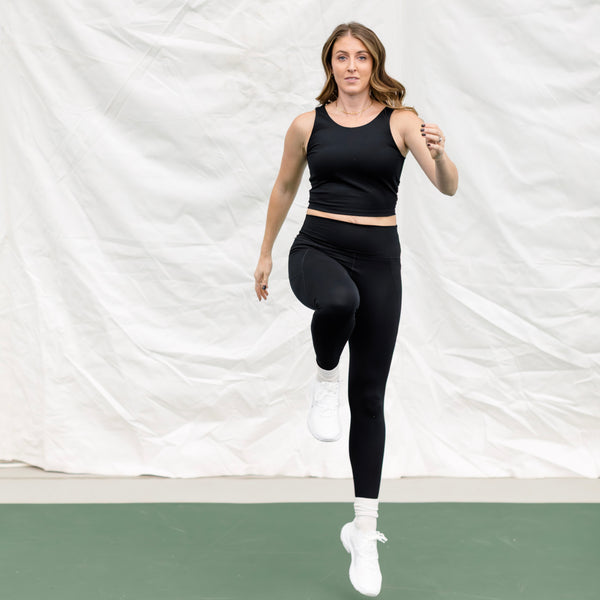 Woman wearing a black athletic set jumping in the air. 